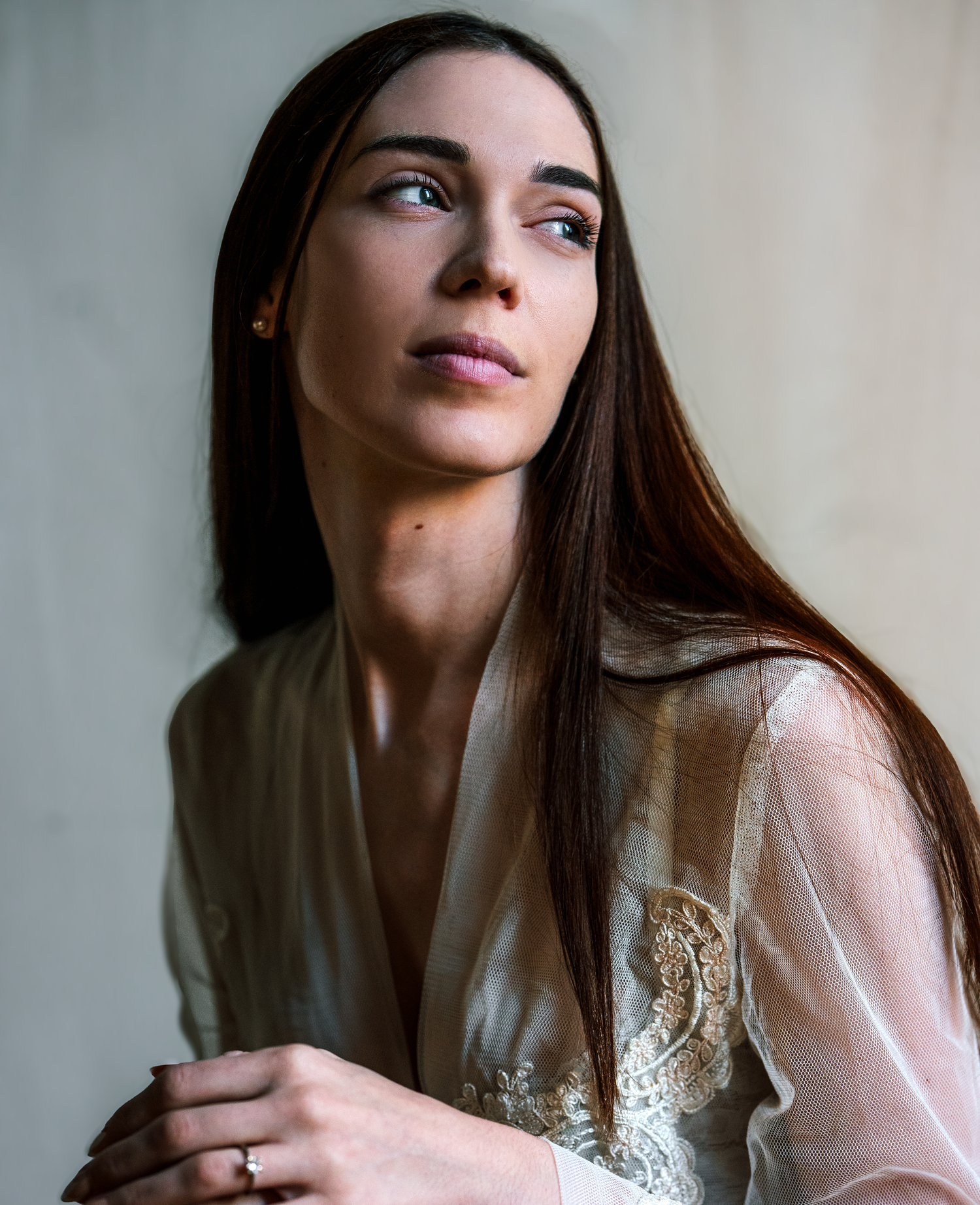 Elegant woman in sheer lace robe with long dark hair gazing upward in soft natural light.
