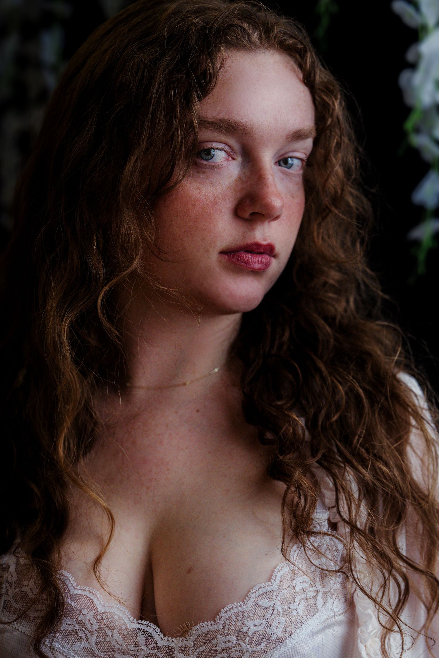 Young woman with curly auburn hair and freckles wearing white lace top, portrait photography.