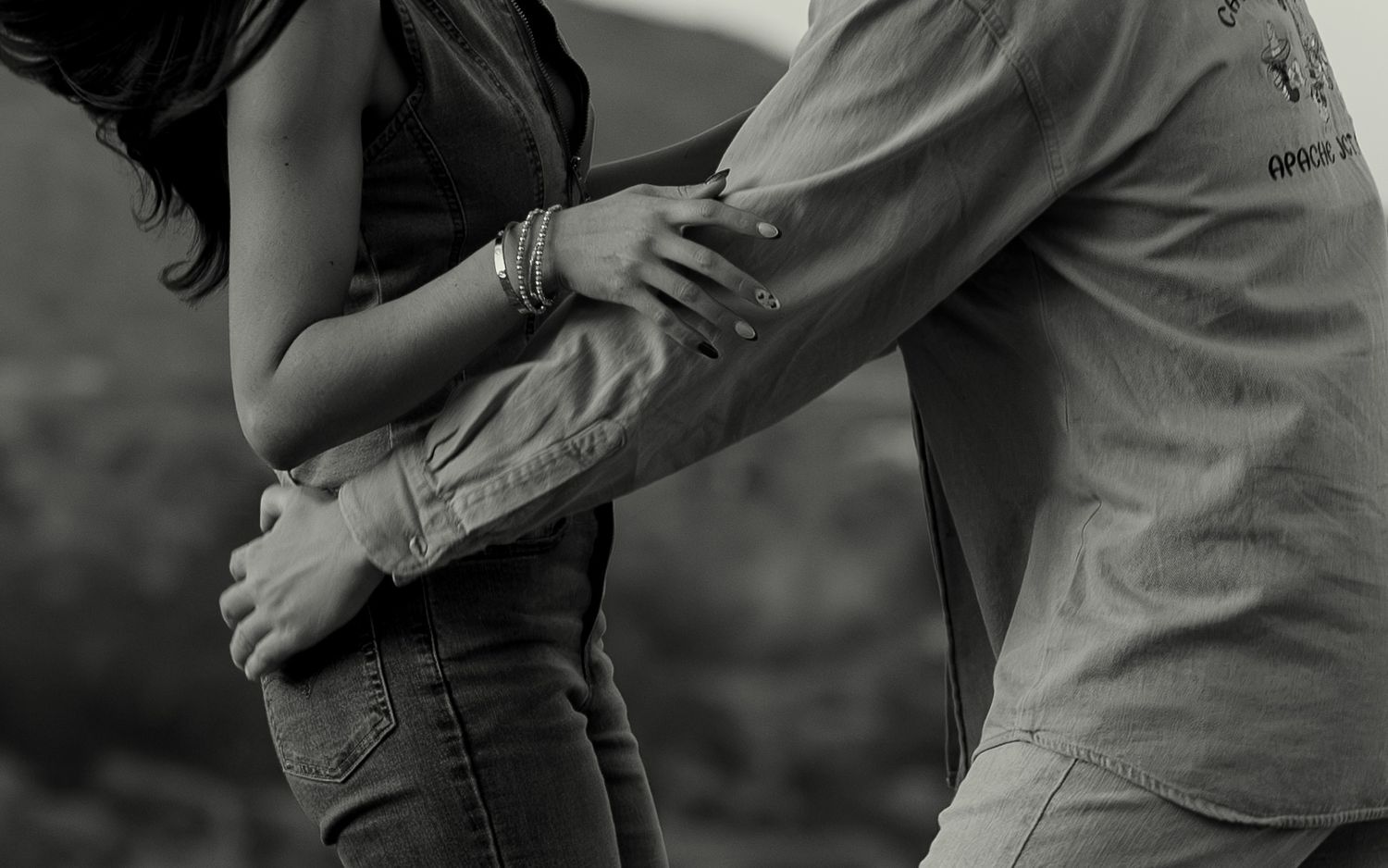 Black and white photo of a couple embracing intimately outdoors, man wrapping arms around woman in jeans.
