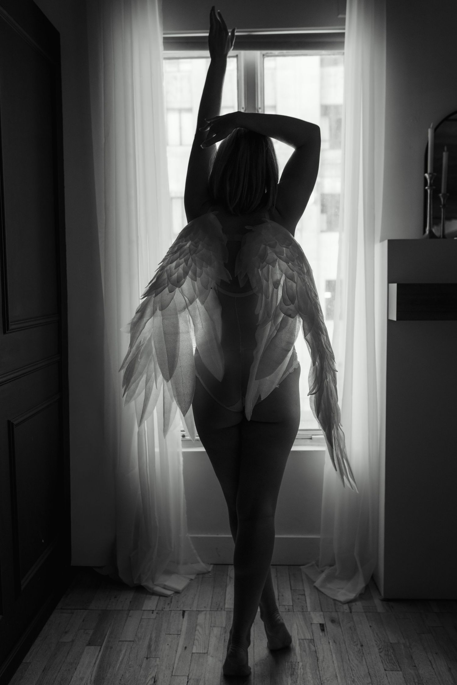 Black and white silhouette of woman with angel wings posing by bright window.
