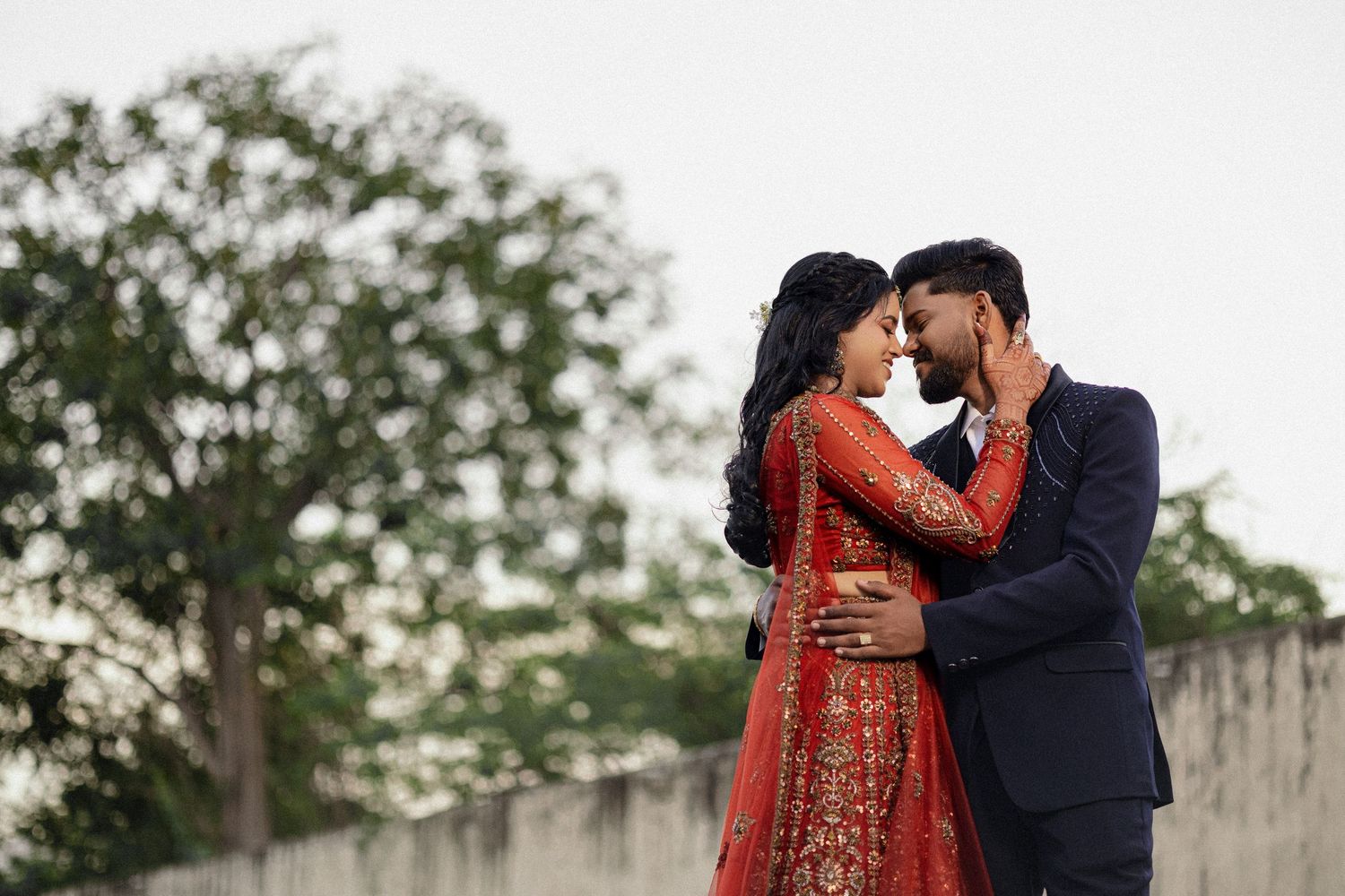 Bride in red saree embracing groom outdoors at dusk, candid wedding photography, Tamil Nadu