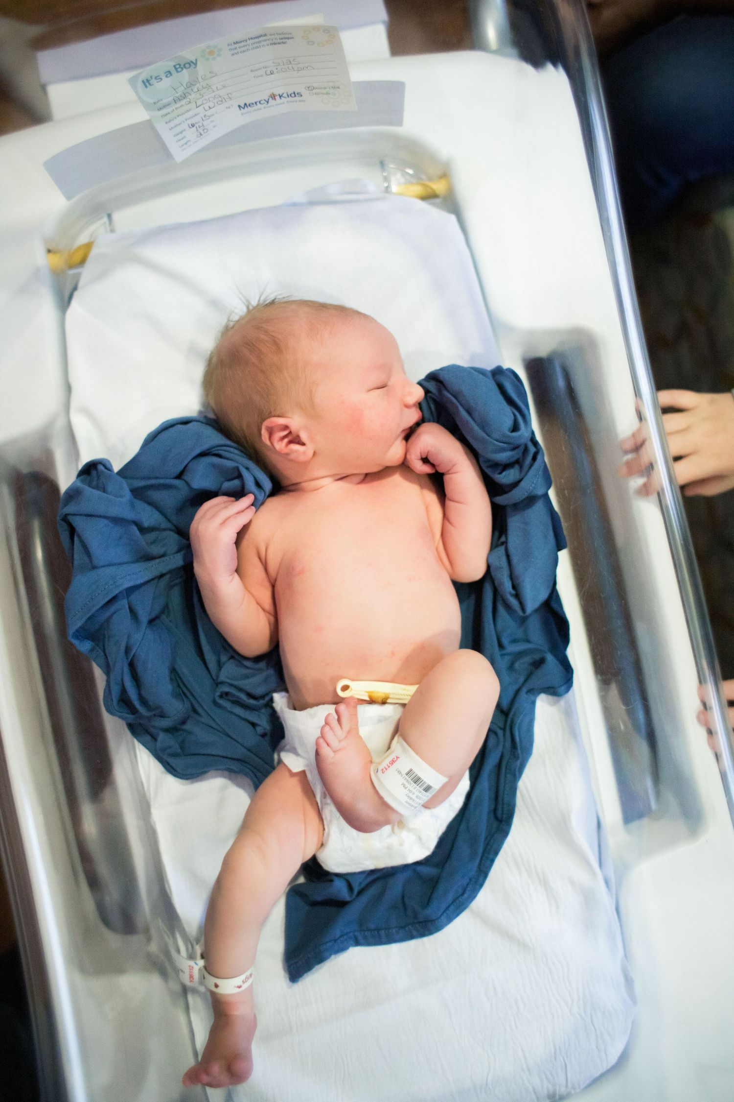 Newborn baby resting in hospital bassinet wrapped in blue blanket after birth.