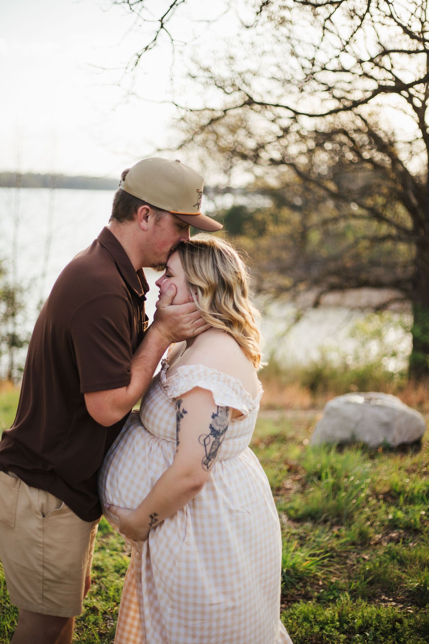 Couple sharing a kiss outdoors during golden hour maternity photo session by a lake.