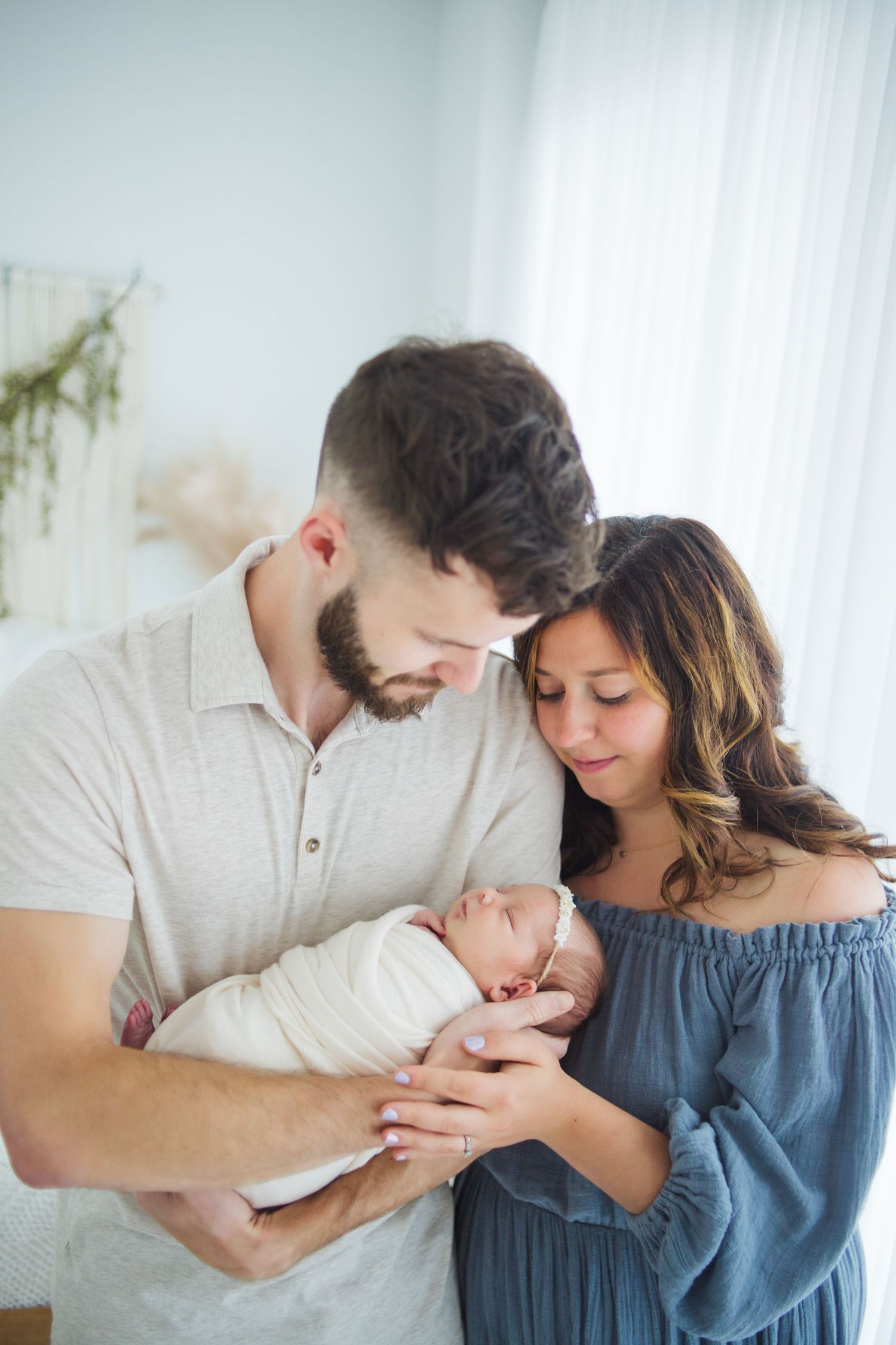 Loving parents gazing at their swaddled newborn baby together near a bright window.