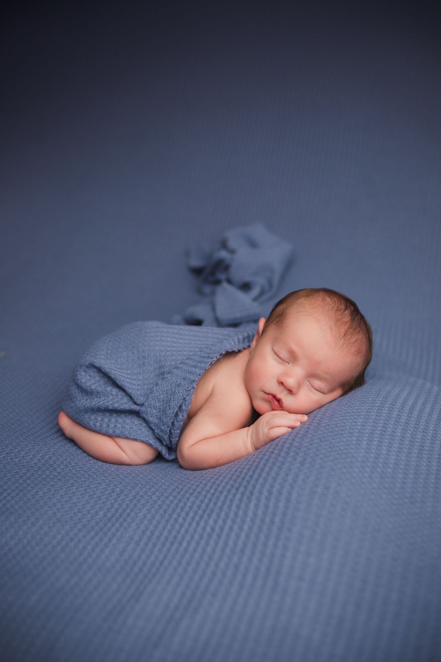 A peaceful newborn sleeps wrapped in a soft blue blanket on a matching background.