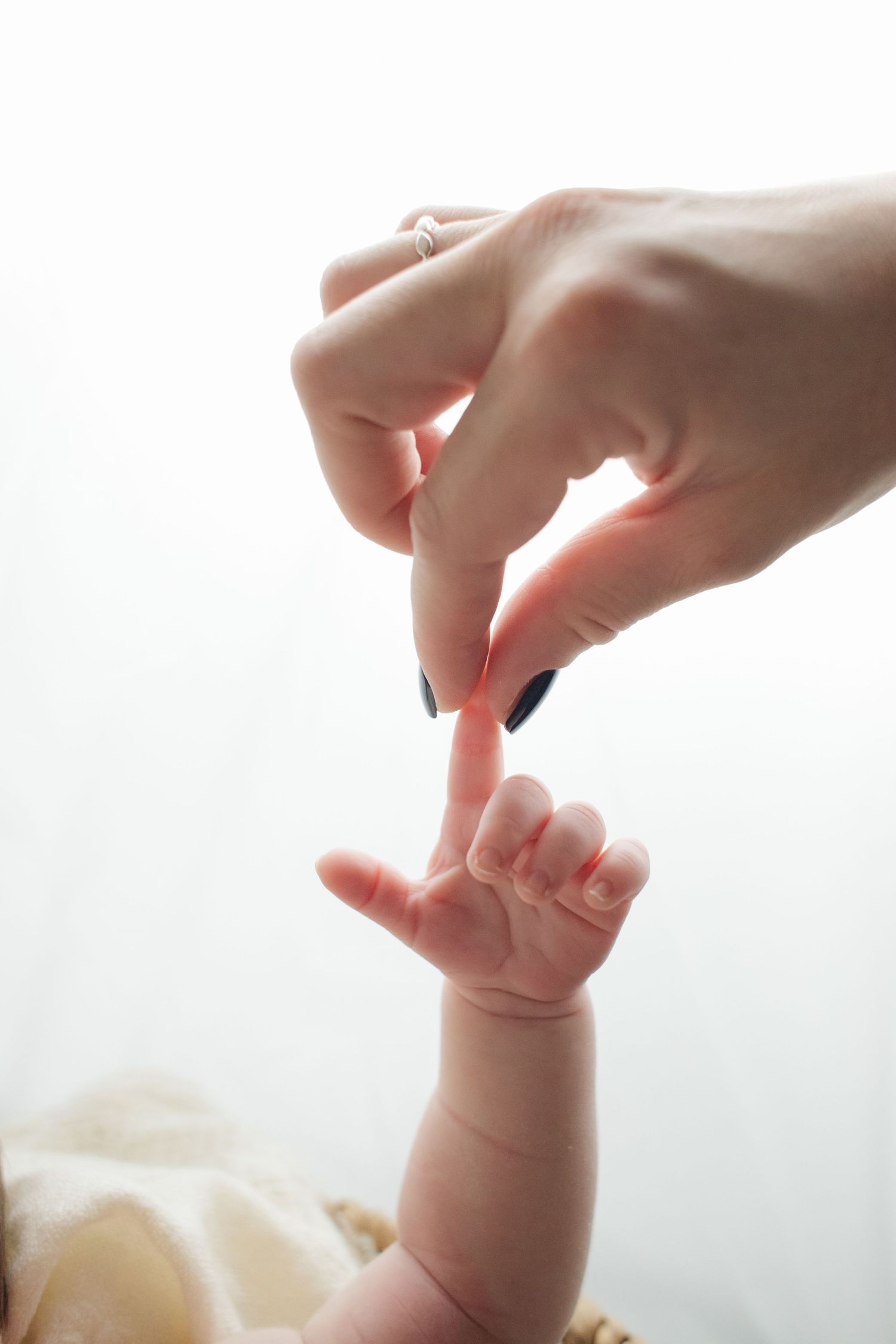 Close-up of mother touching fingertips with sleeping newborn baby, ring visible on hand.