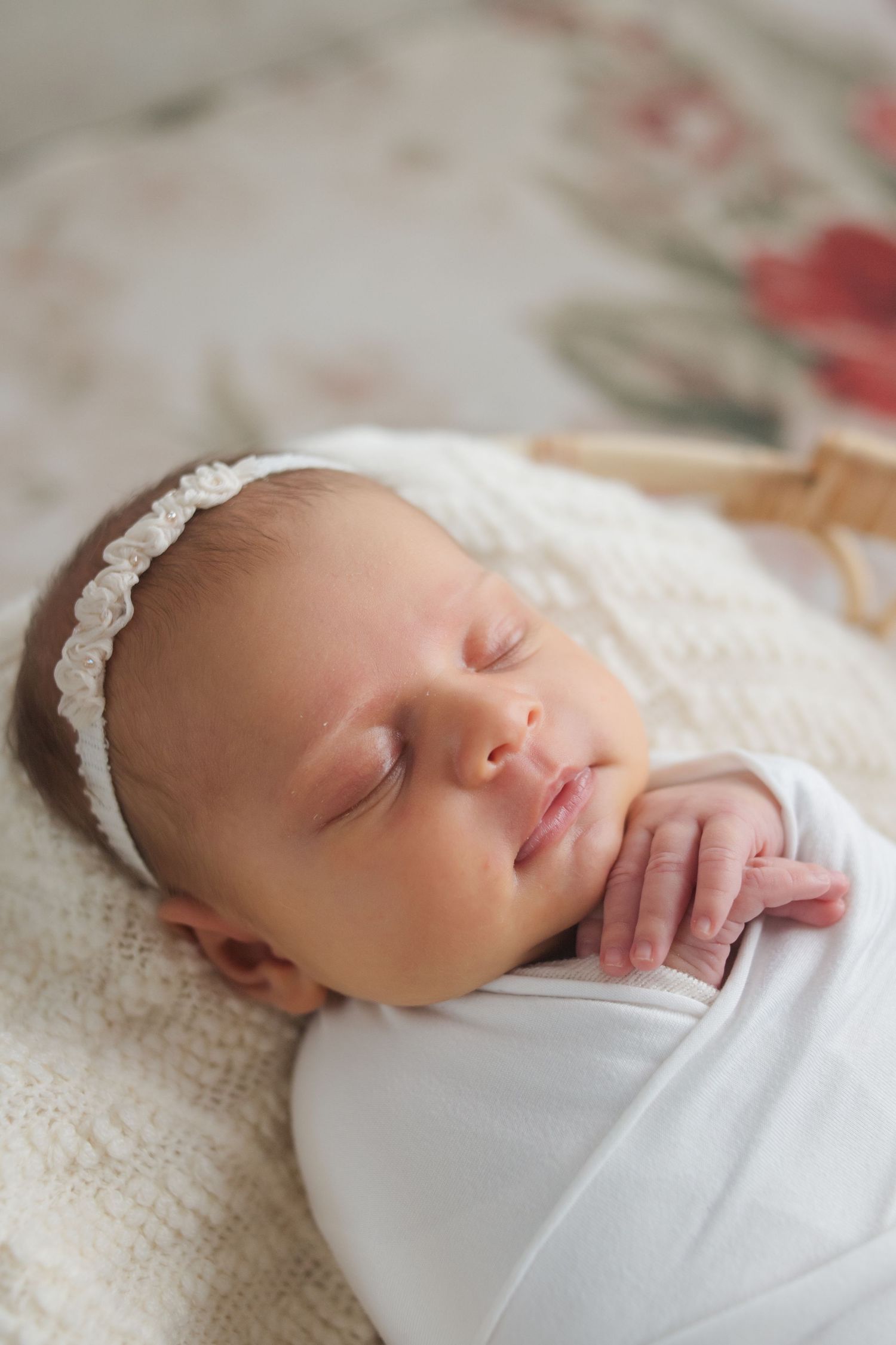 Peaceful newborn baby girl sleeping swaddled in white with a delicate floral headband.