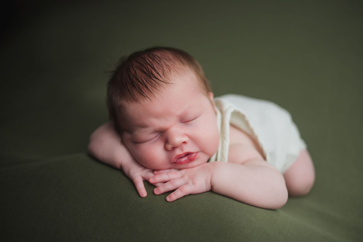Smiling newborn baby posed on green backdrop during professional newborn photography session.