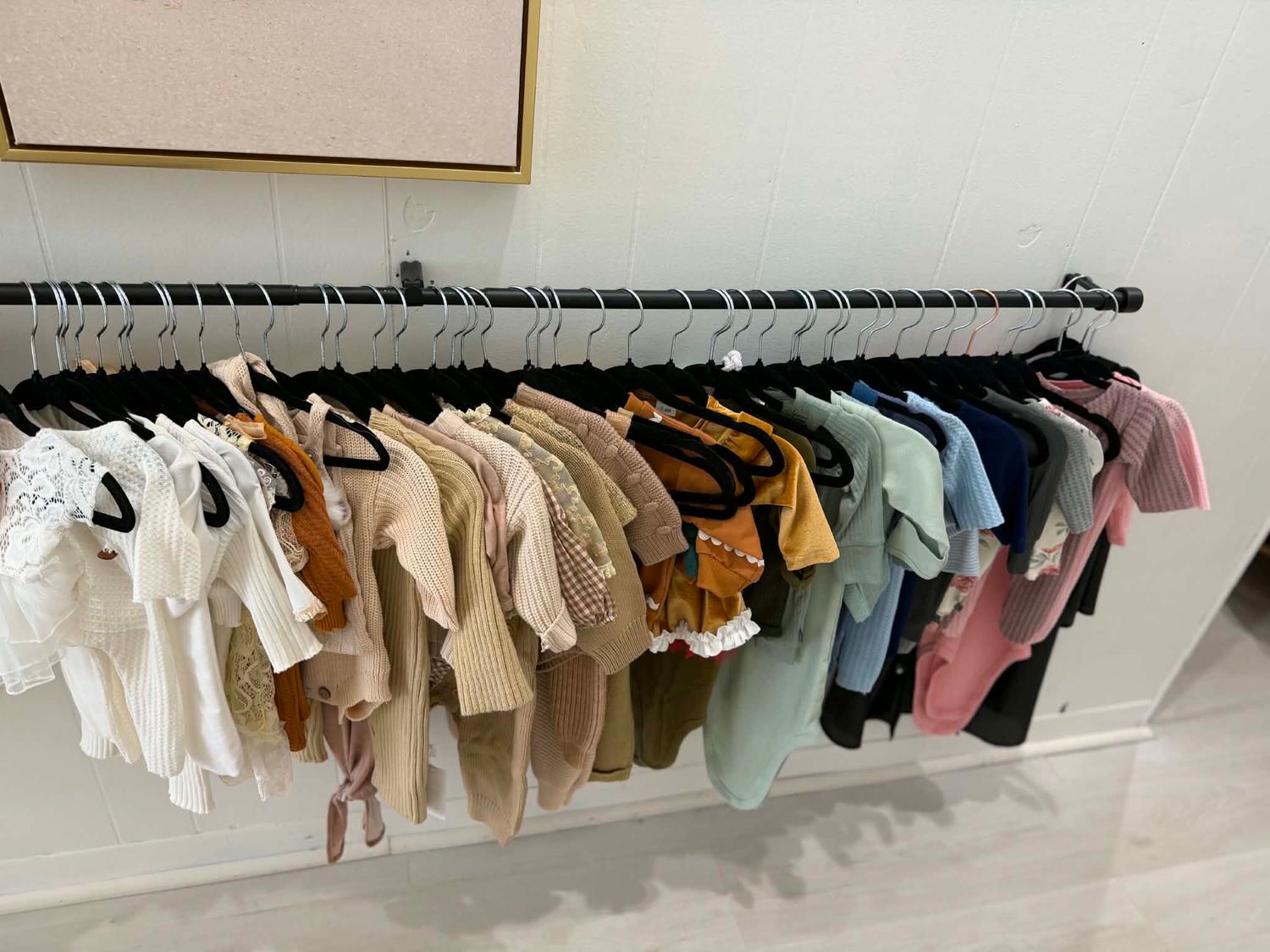 A wall-mounted clothing rack displaying an assortment of colorful children's garments on black hangers in a bright room.