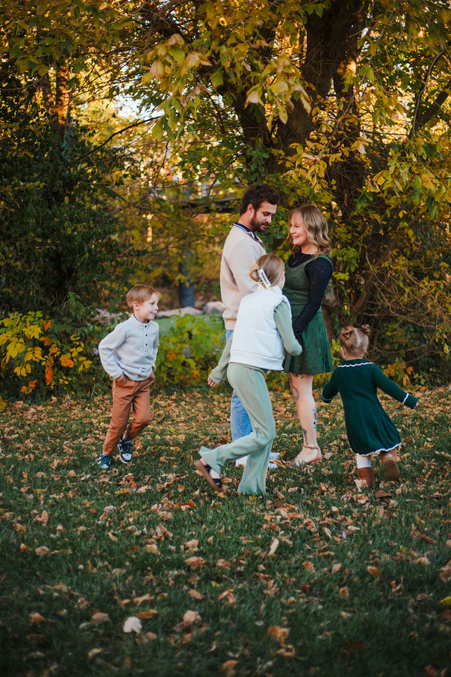 Family of five enjoying autumn park, parents gazing lovingly while three children play around them.