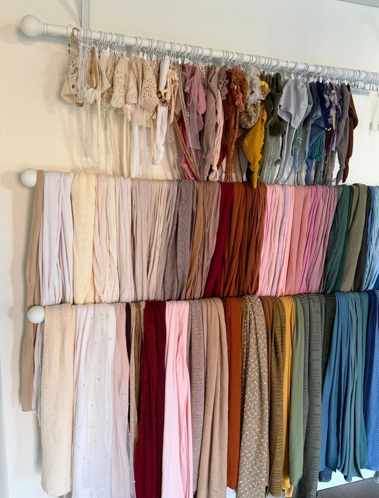 A organized display of colorful fabric wraps and textiles hanging on a rod in a photography studio.