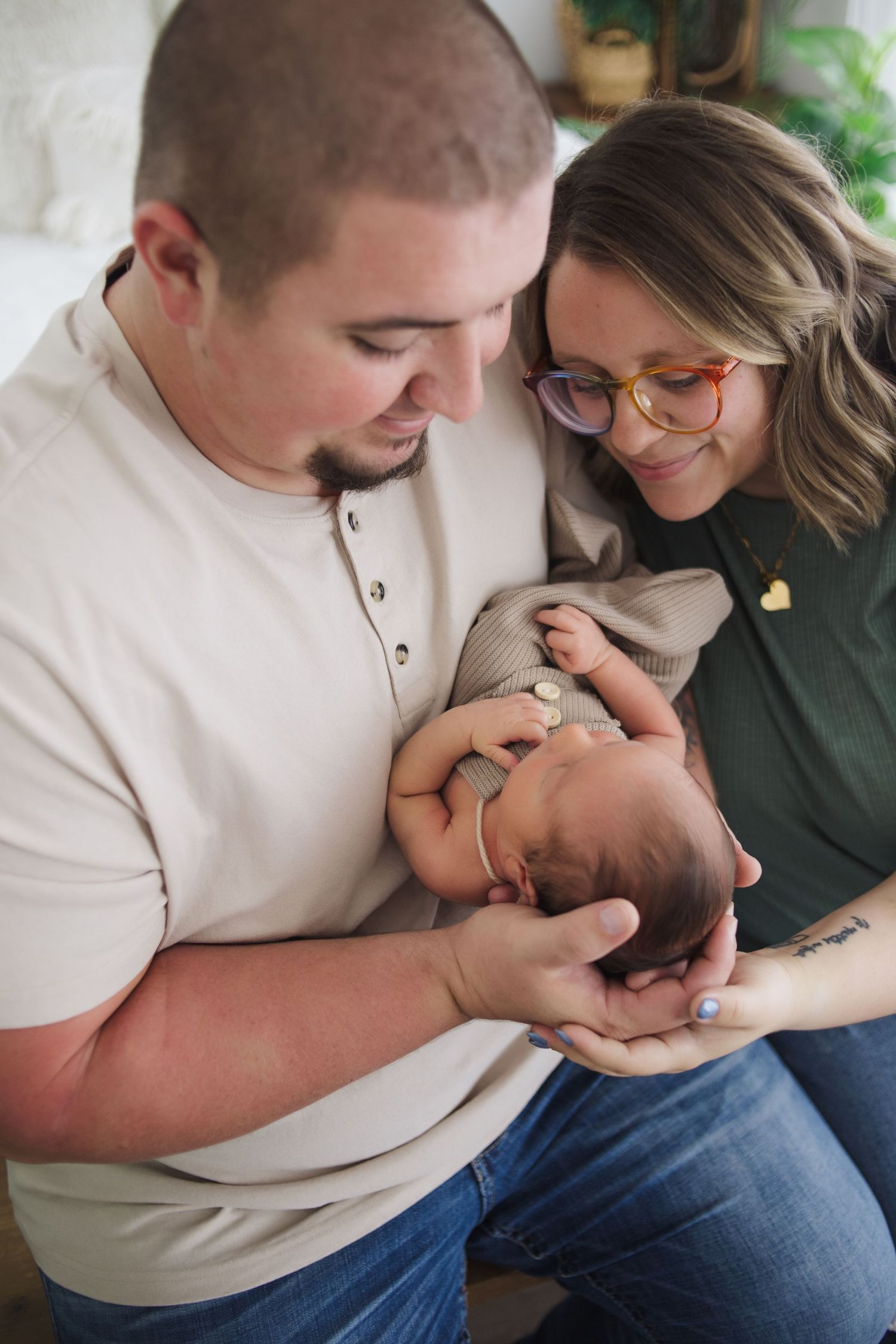 New parents smiling and cradling their newborn baby during professional newborn photo session.