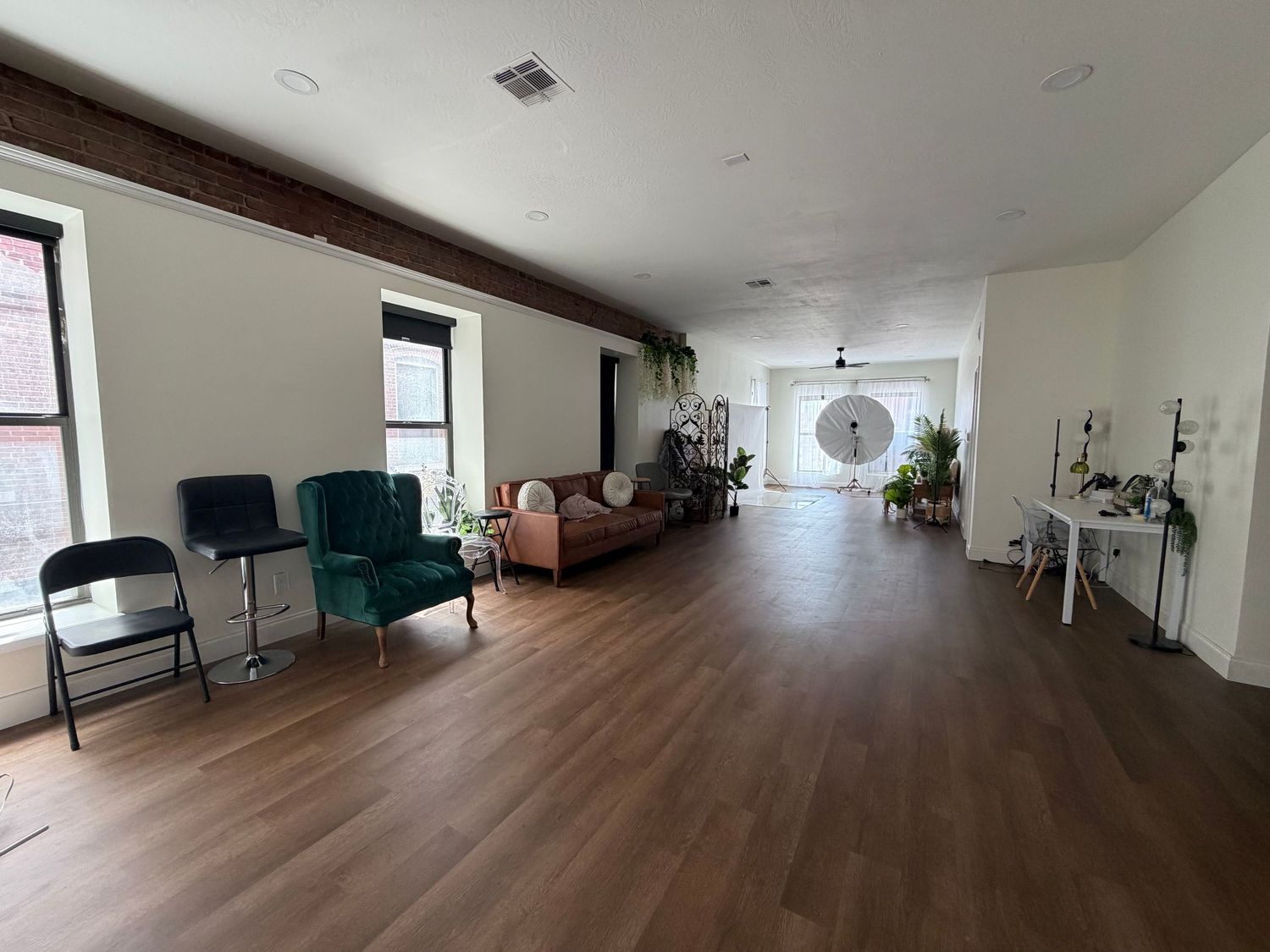 A spacious photography studio with hardwood floors, seating area, and natural light from large windows.