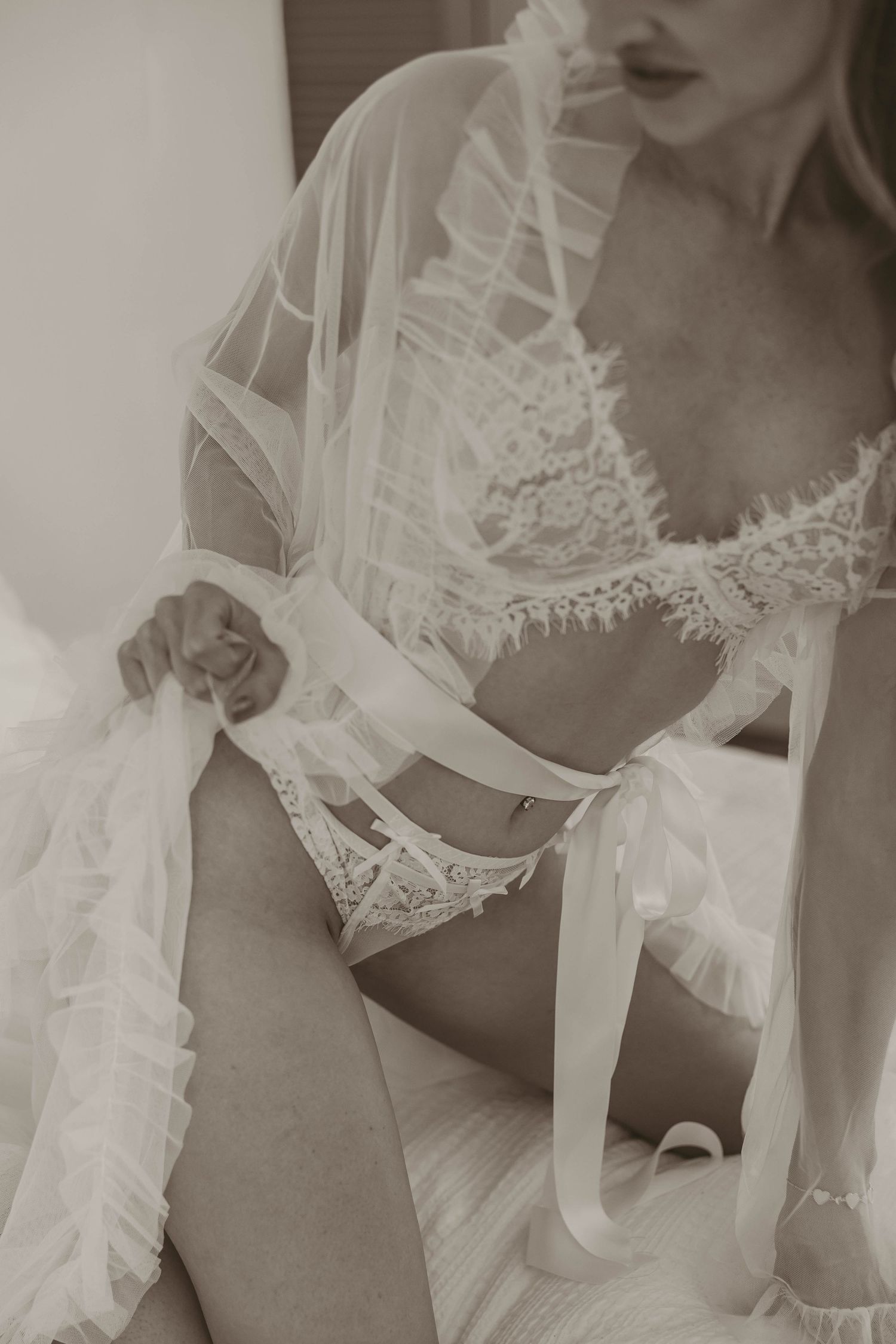 Elegant bridal boudoir photo featuring white lace lingerie and sheer robe in a soft sepia tone.