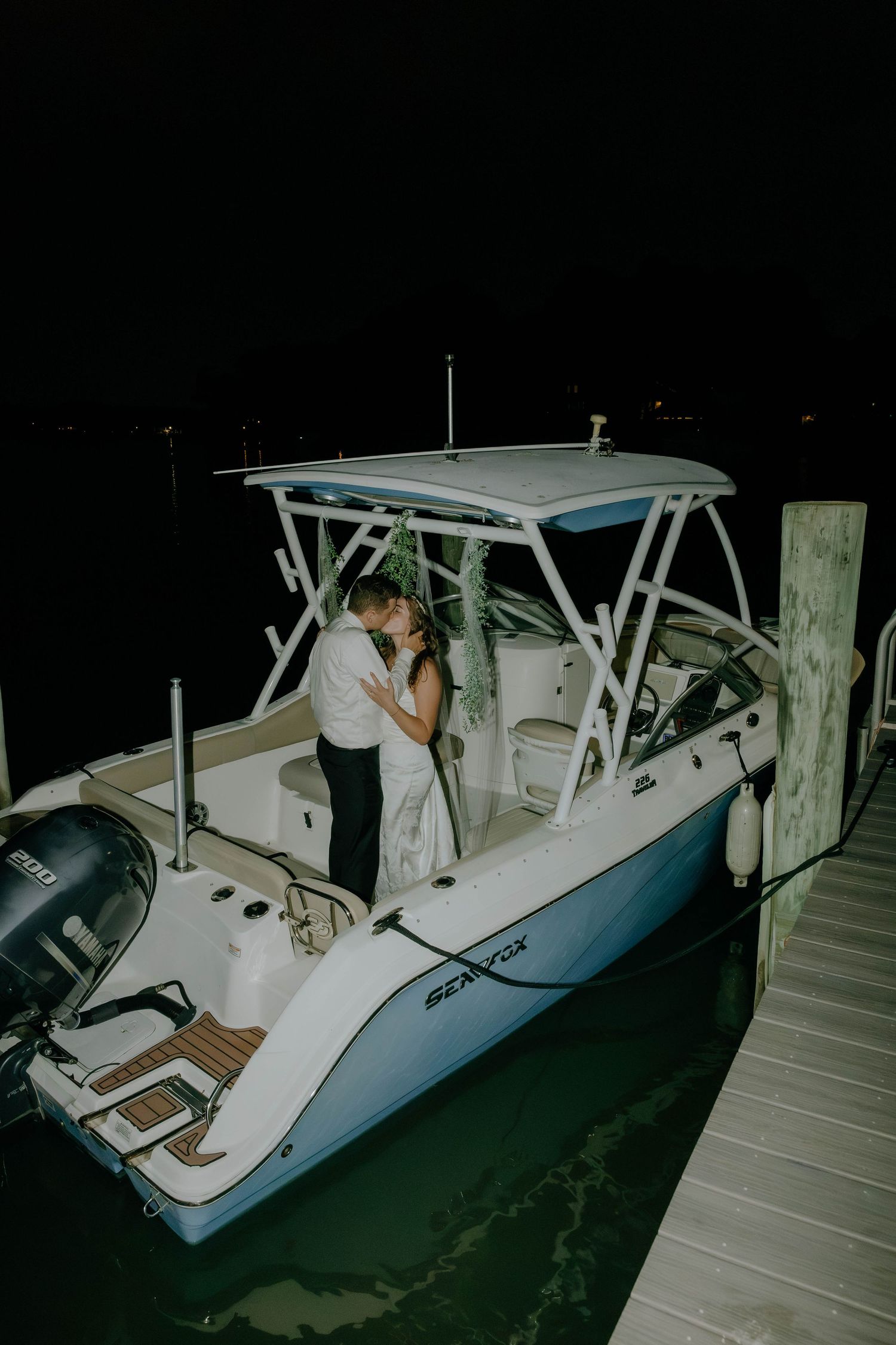Newlyweds sharing a romantic kiss on a Sea Fox boat docked at night after their wedding celebration.