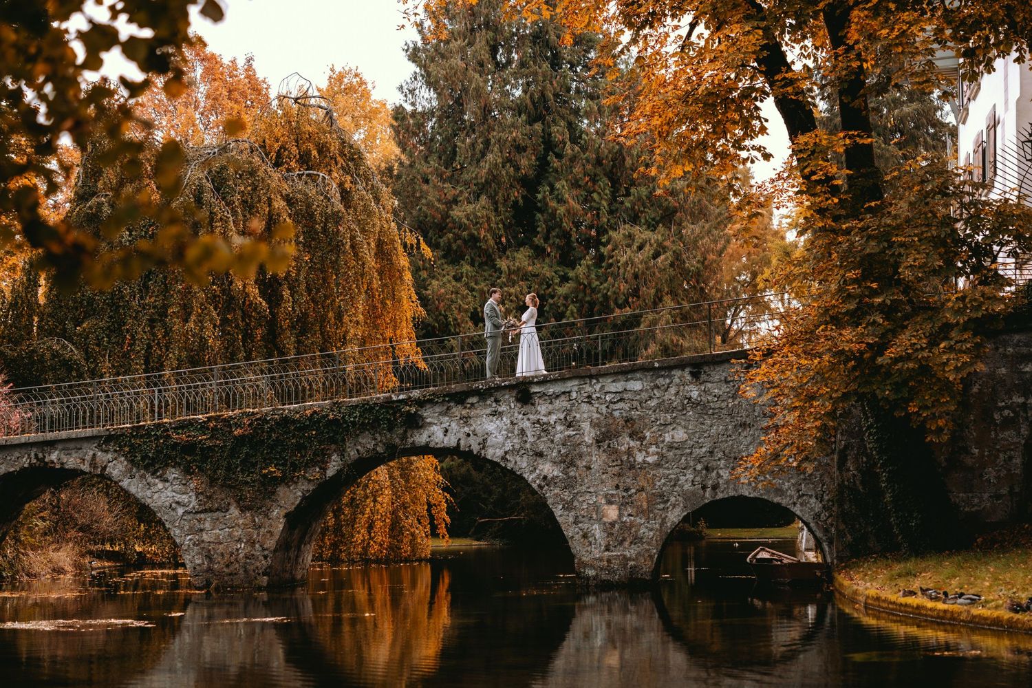 Brautpaar steht auf einer malerischen Steinbrücke im Herbst. Epische und natürliche Hochzeitsfotografie in der Schweiz.