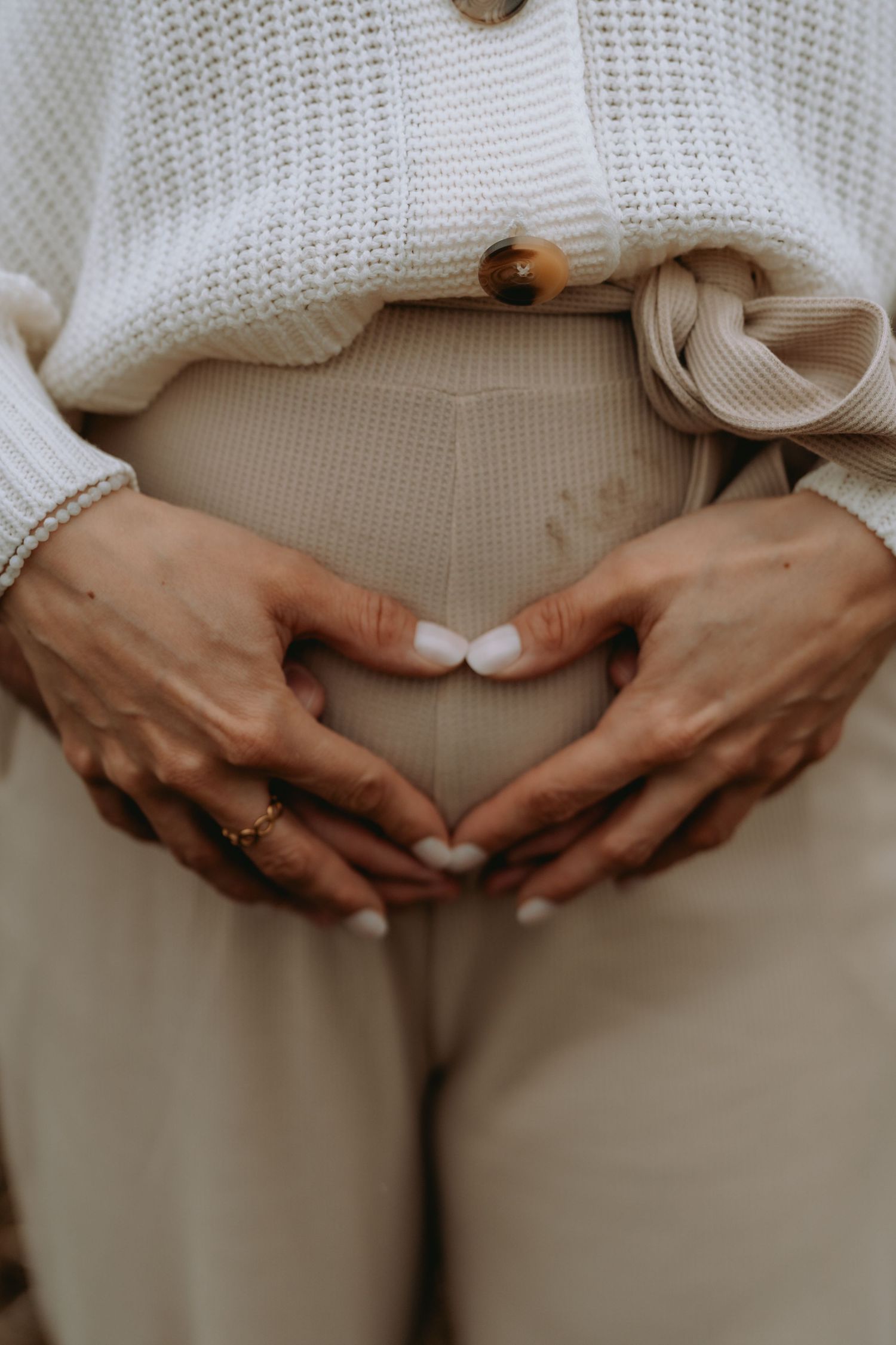 Zwei Hände formen ein Herz auf dem Babybauch. Natürliche Schwangerschafts-Shootings am Inkwilersee, Solothurn.