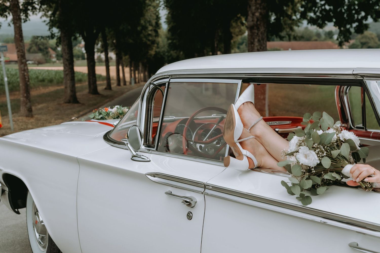 Braut lässt Beine mit Brautstrauss aus einem Oldtimer baumeln. Authentische Hochzeitsfotografie Solothurn.