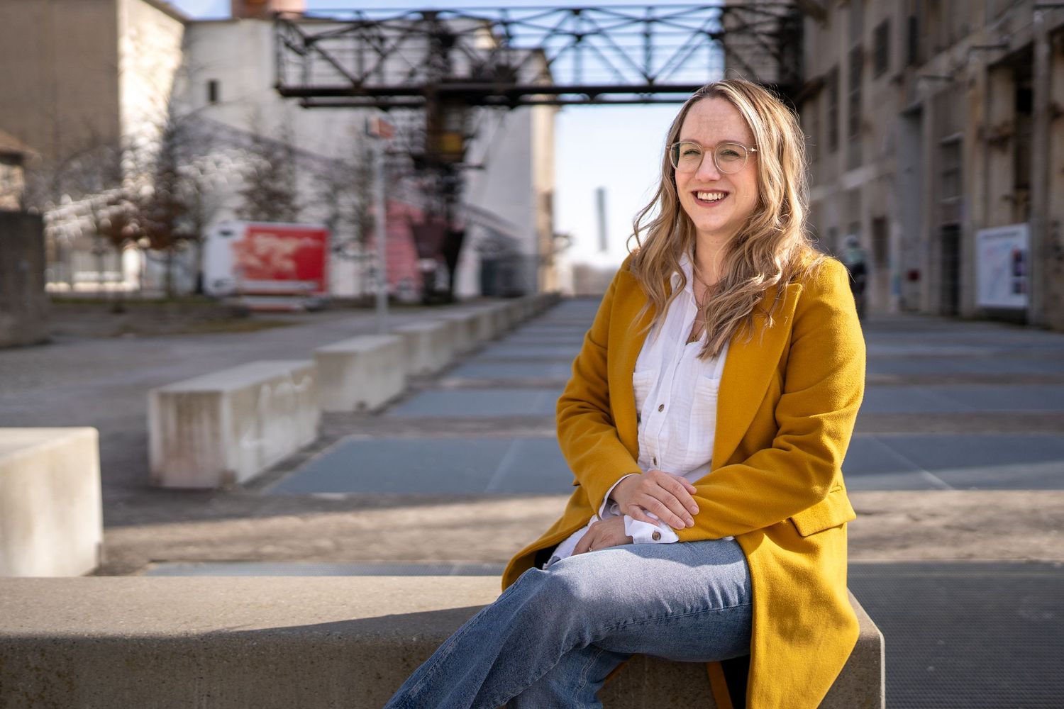 Lachende Frau im gelben Mantel sitzt in einer urbanen Kulisse. Authentische Business-Porträts und Personal Branding Solothurn.