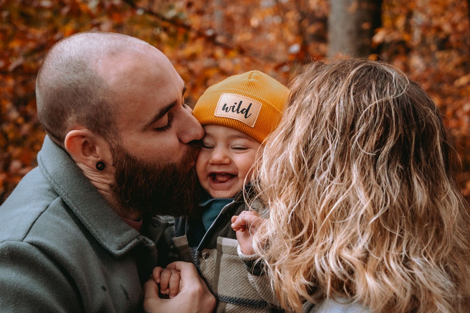 Vater gibt seinem Kind im Herbstwald einen Kuss auf die Wange. Natürliche, lebendige Familienfotos Solothurn.
