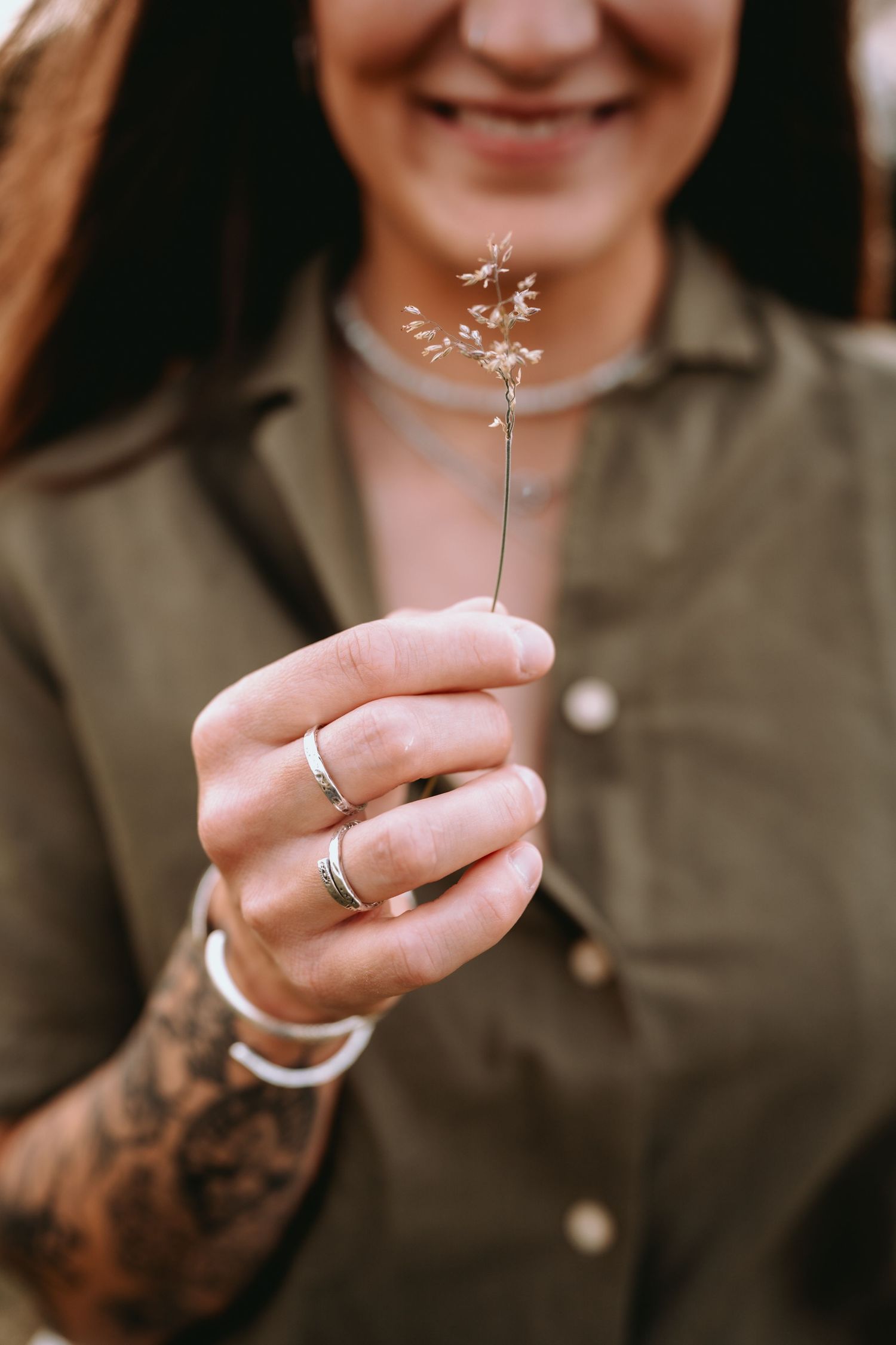 Frau mit Tattoos hält lächelnd eine kleine Blume in der Hand. Entspannte Porträtfotografie und Business-Shootings Solothurn.