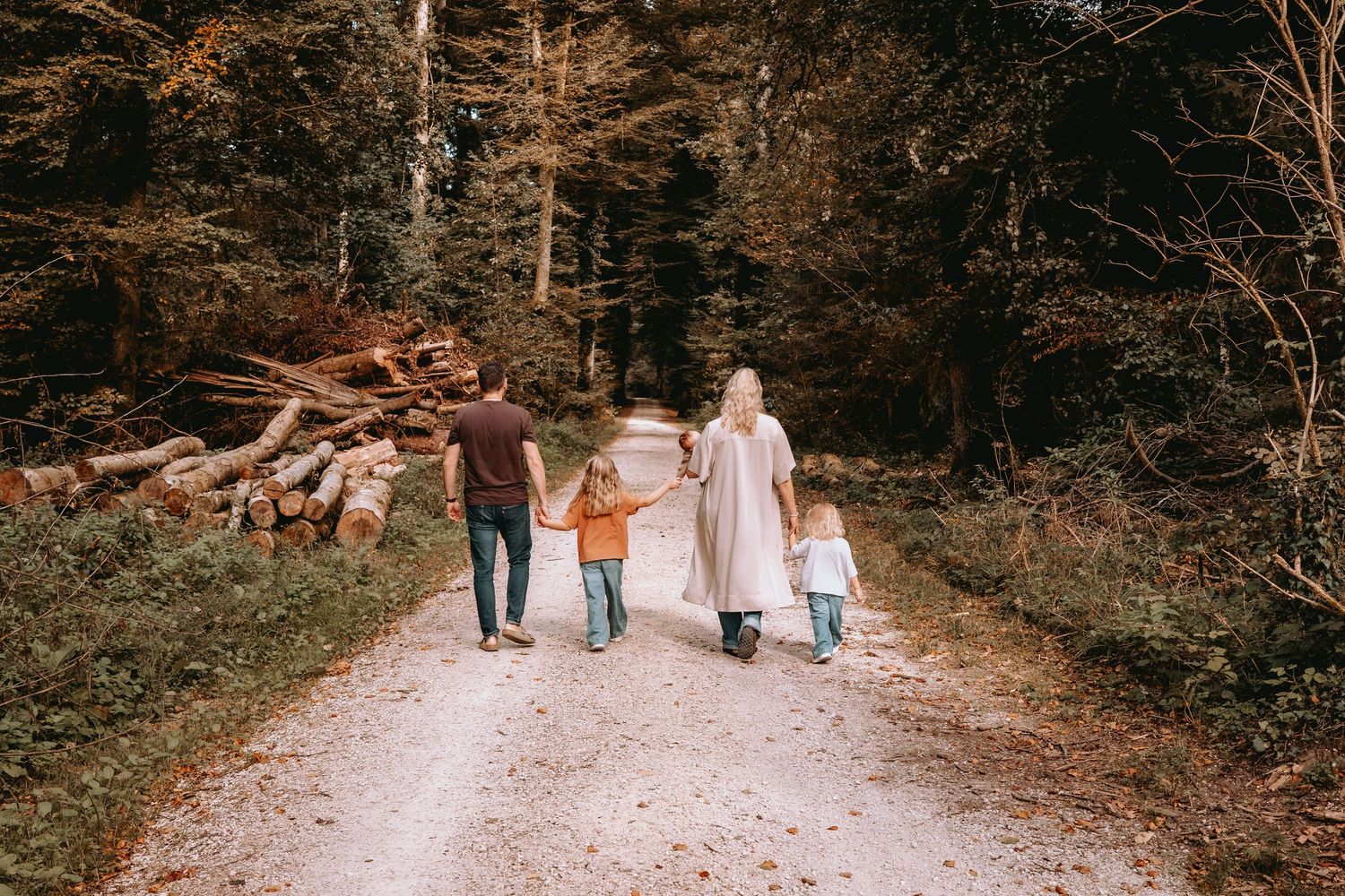 Familie läuft Hand in Hand einen Waldweg im Herbst entlang. Ungestellte Familienfotos und Outdoor-Shootings.