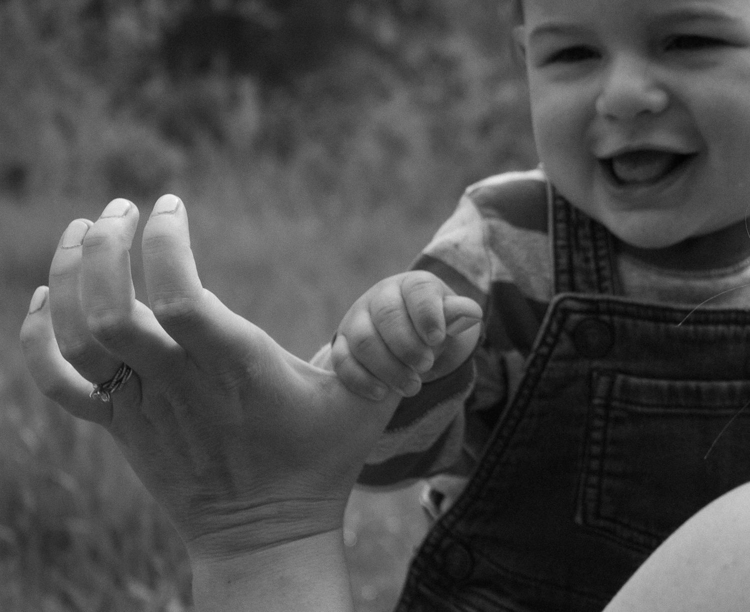 Black and white photo of a laughing baby holding an adult hand outdoors.