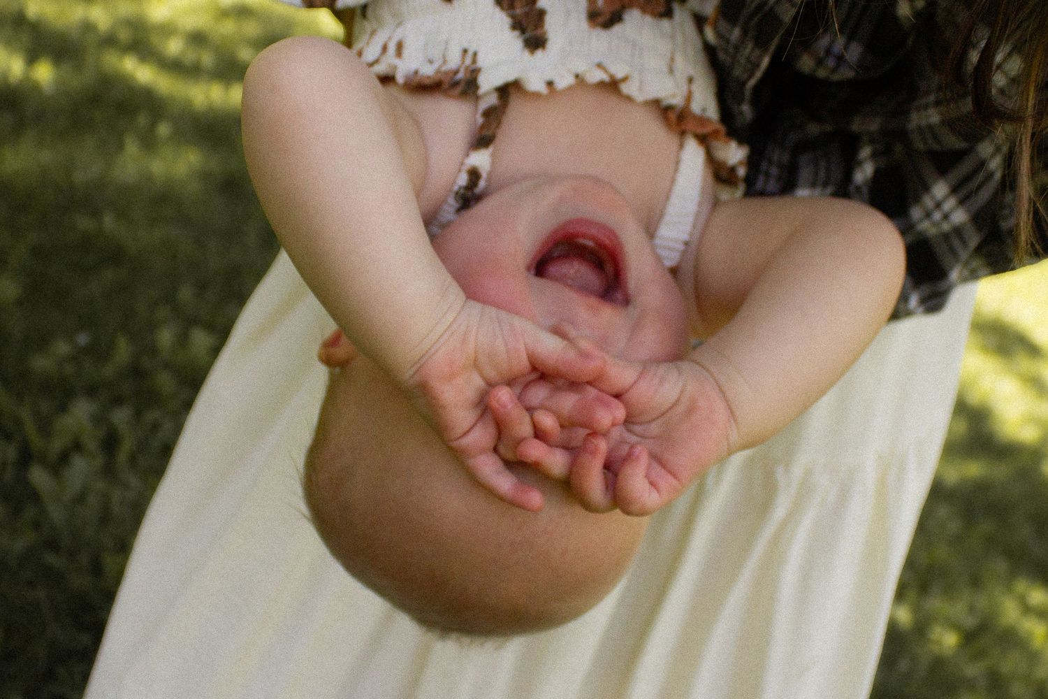 Baby being held upside down laughing with tiny hands visible outdoors in garden.