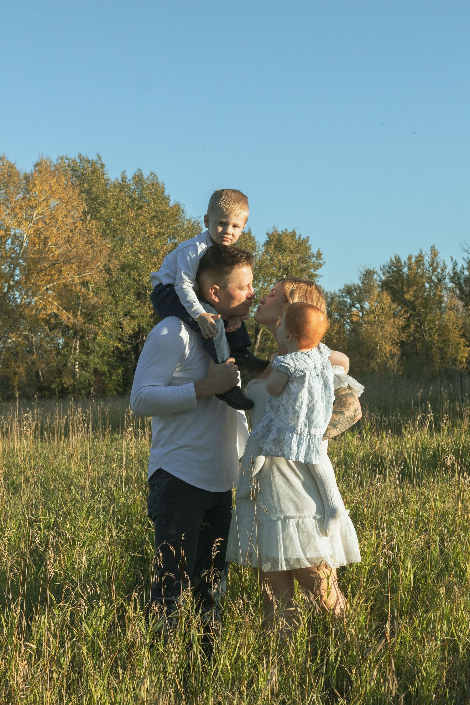 Happy family with two young children enjoying a sunny day in a green meadow with autumn trees in the background.