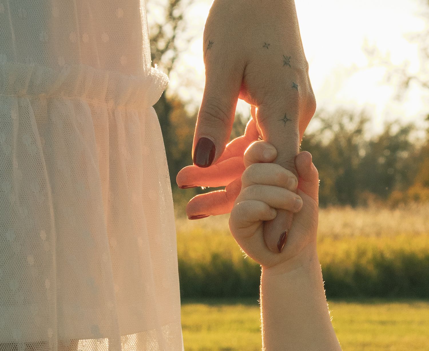 A mother gently holds her child's hand outdoors in warm golden sunlight, symbolizing love and connection.