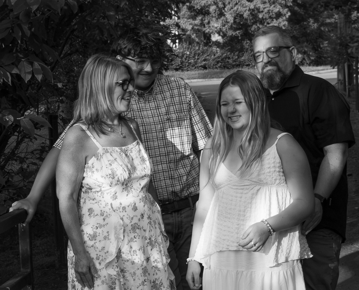 Black and white photo of four smiling family members posing together outdoors near green foliage.
