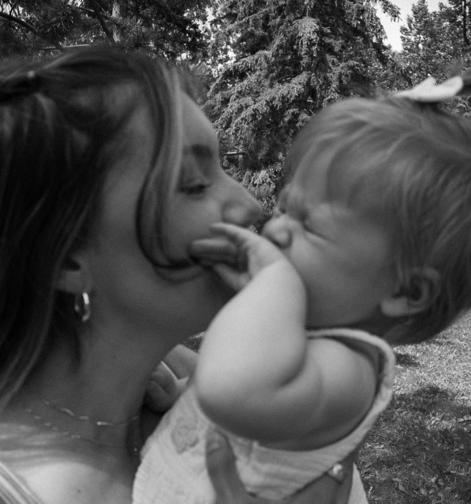 Black and white photo of mother kissing baby girl with white bow in hair.