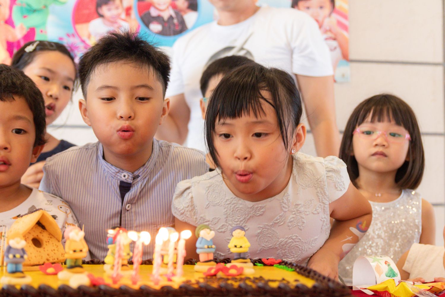 Children blowing out birthday candles on a decorated cake at a festive birthday party celebration.