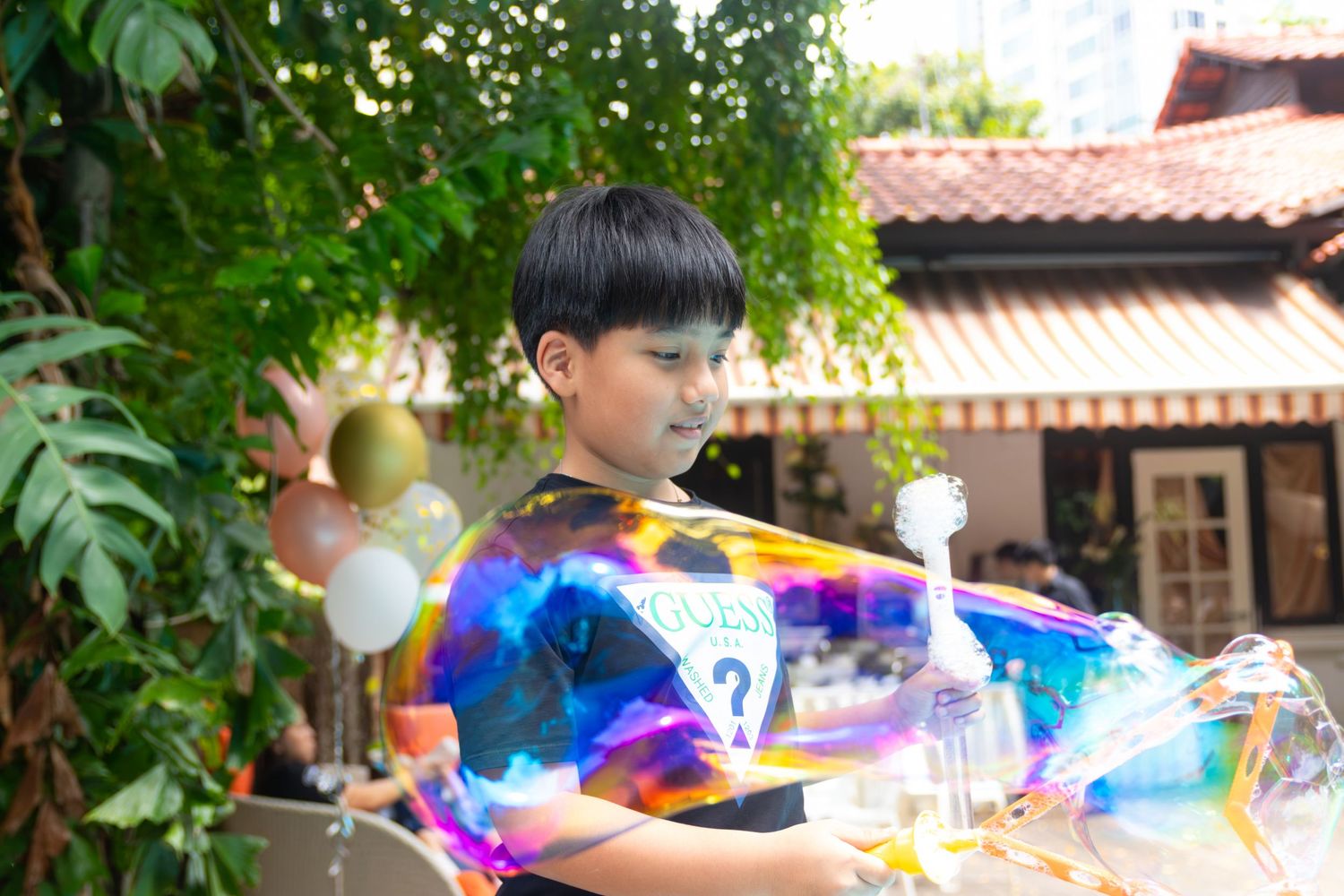 Young boy playing with a large colorful soap bubble outdoors at a festive garden party.