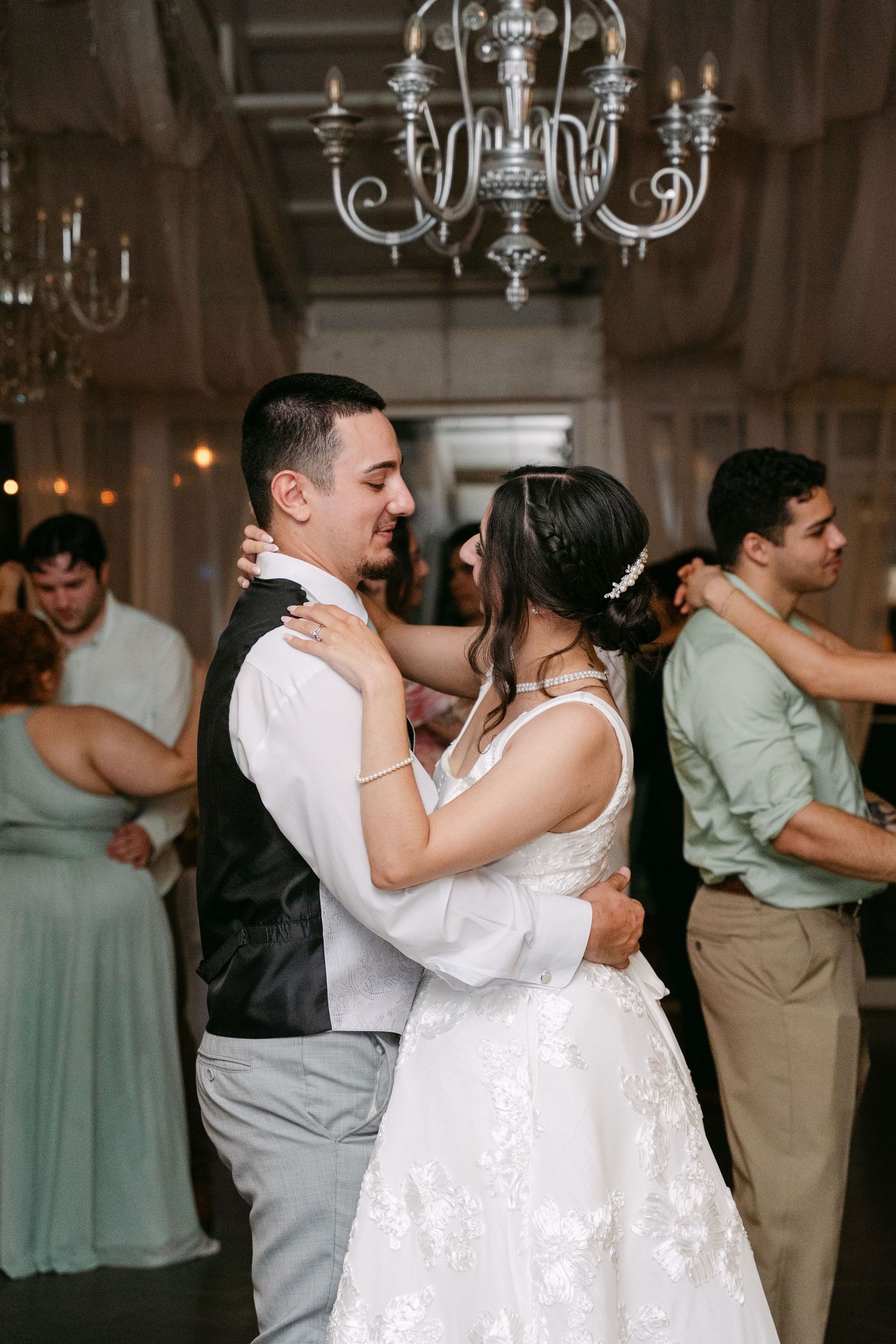 Bride and groom share first dance under chandelier at elegant wedding reception.