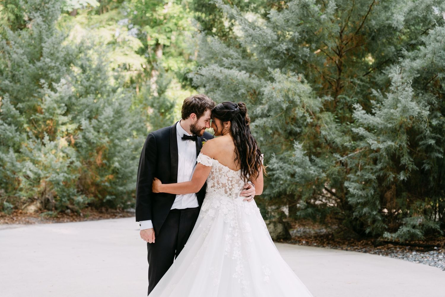 Bride and groom sharing a tender moment surrounded by lush green trees on their wedding day.