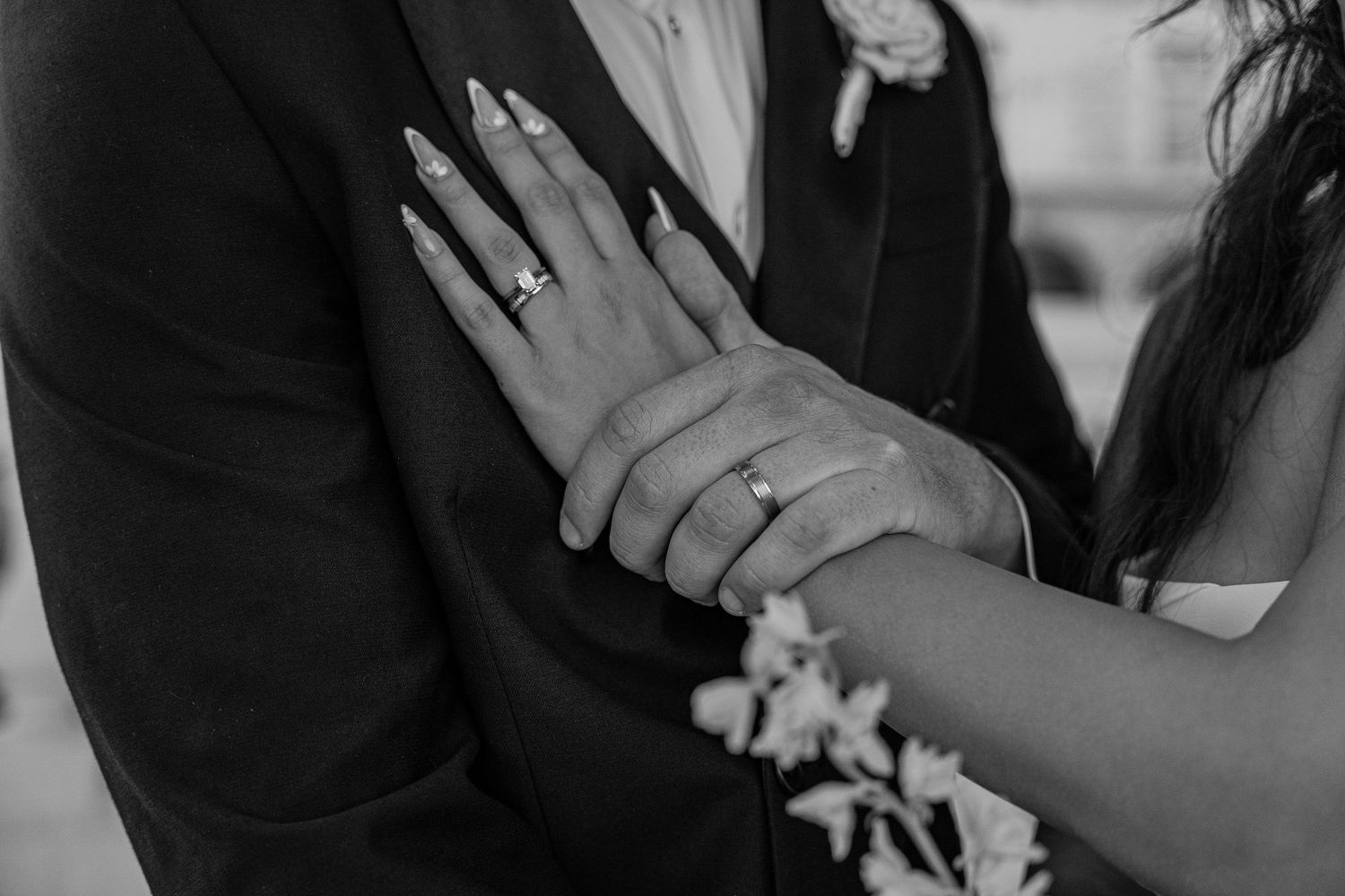 Close-up black and white photo of bride and groom showing off wedding rings with manicured nails.