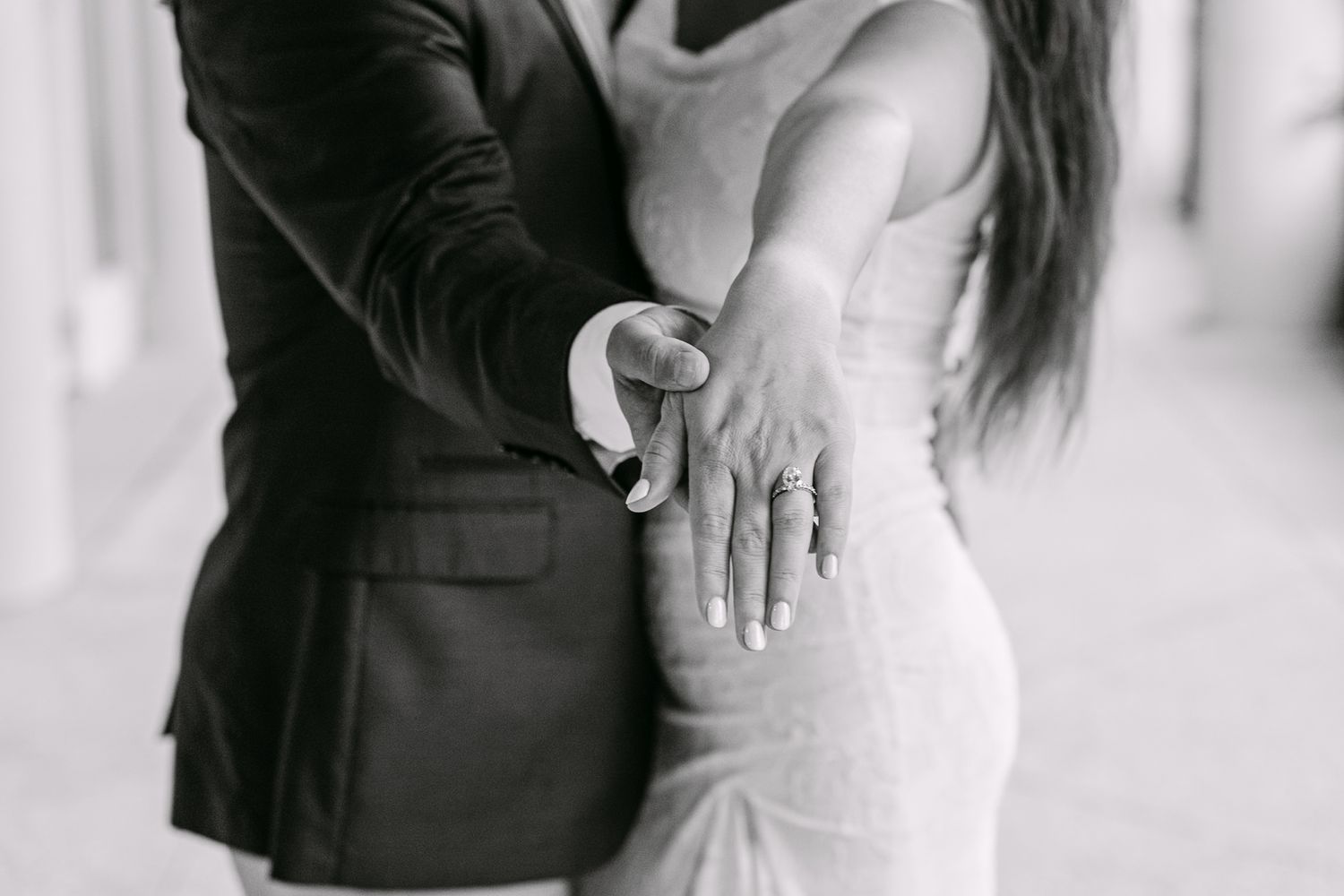 Close-up black and white photo of couple embracing, showcasing a stunning diamond engagement ring.