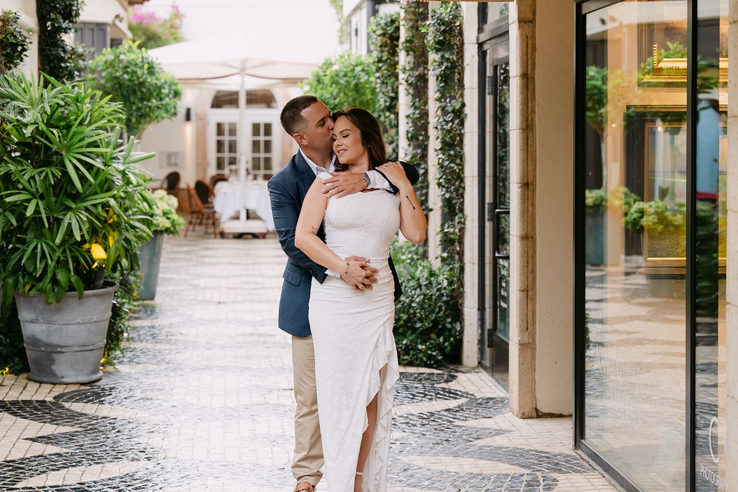 Couple embracing romantically on a decorative mosaic courtyard surrounded by lush tropical greenery.