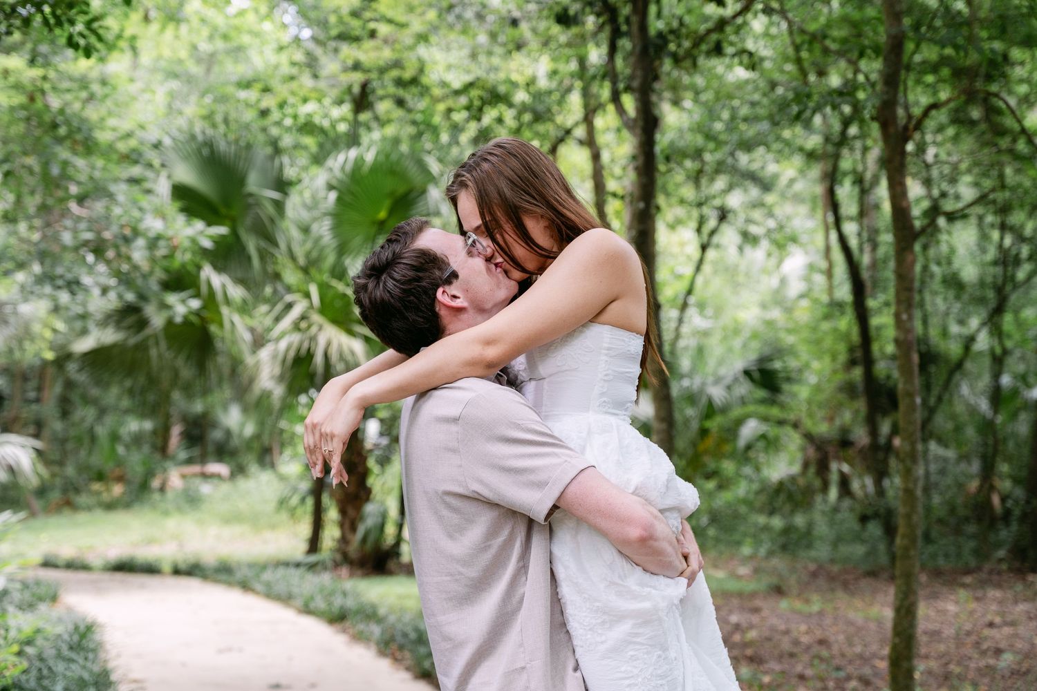 Couple embracing in a lush green garden, man lifting woman in a romantic outdoor setting.