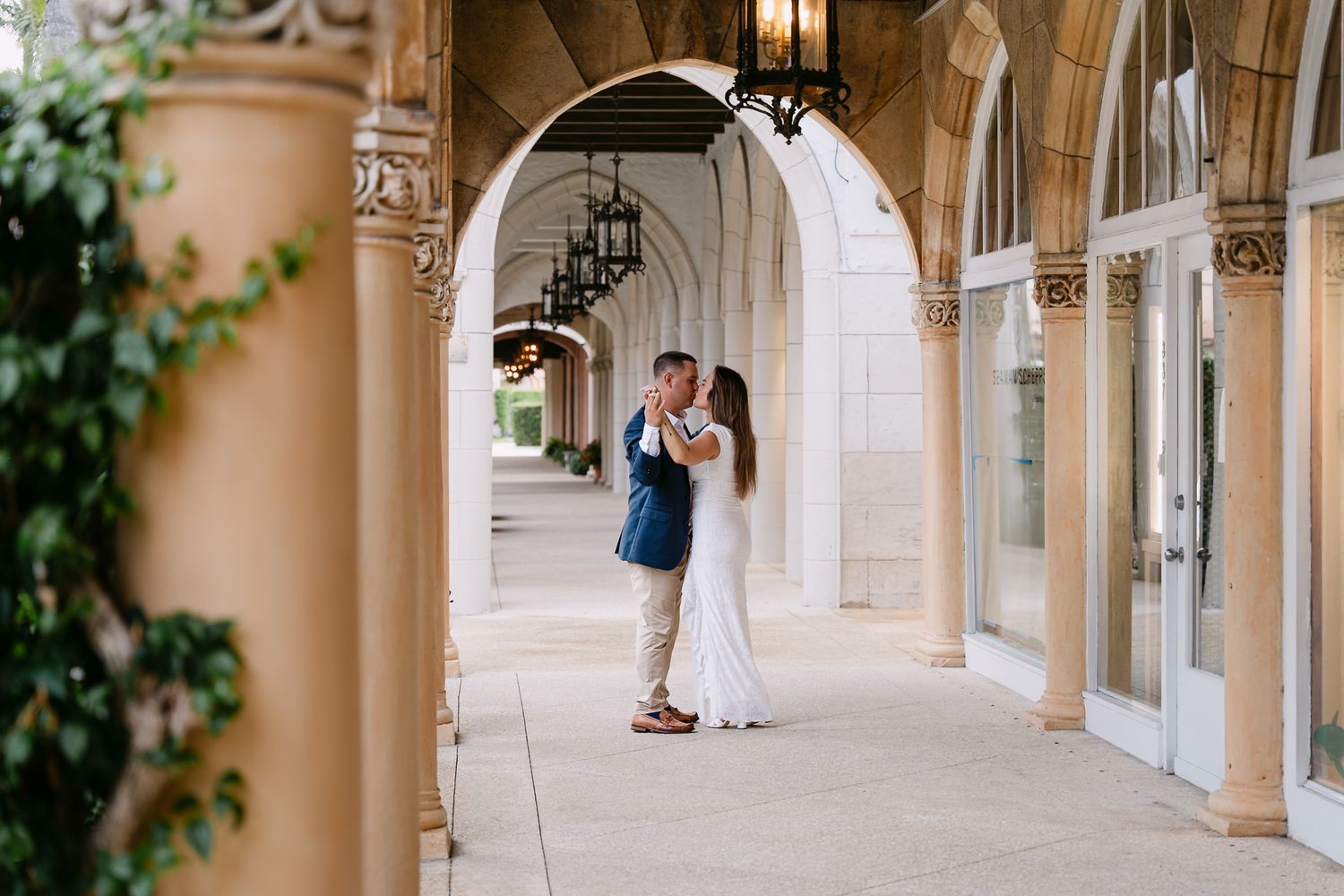 Couple sharing a passionate kiss under elegant stone arches with ornate lanterns in a grand corridor.