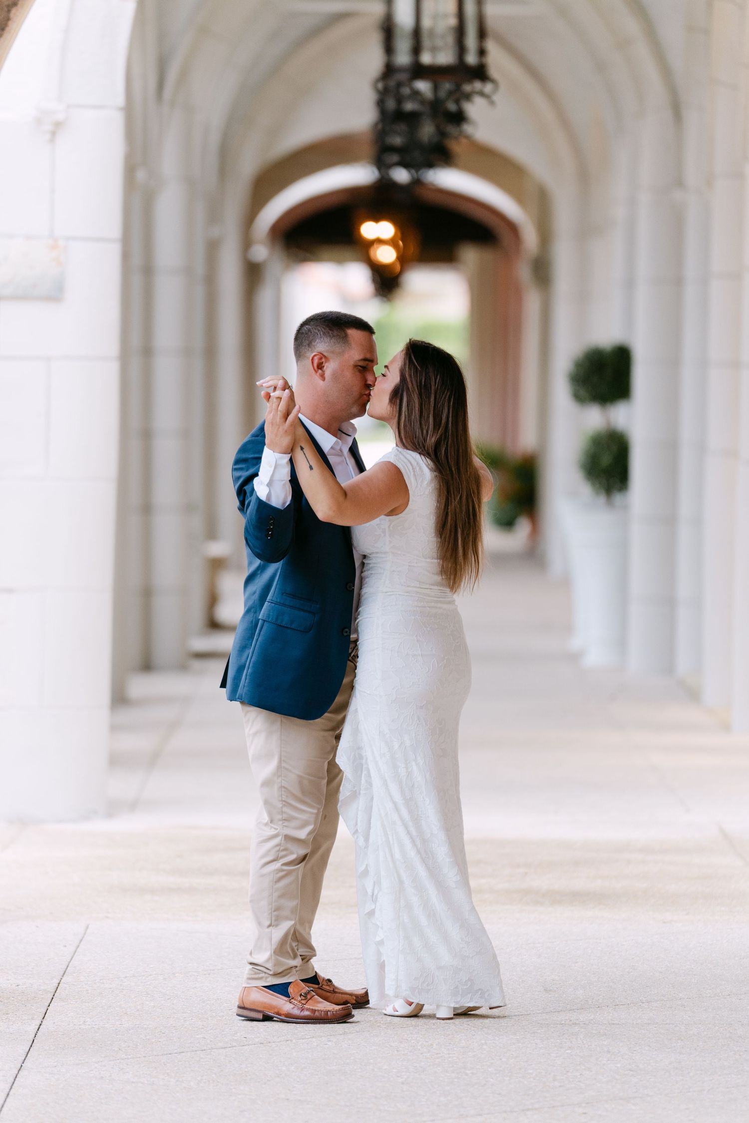 Couple sharing a tender kiss while dancing in a grand white arched corridor during engagement shoot.