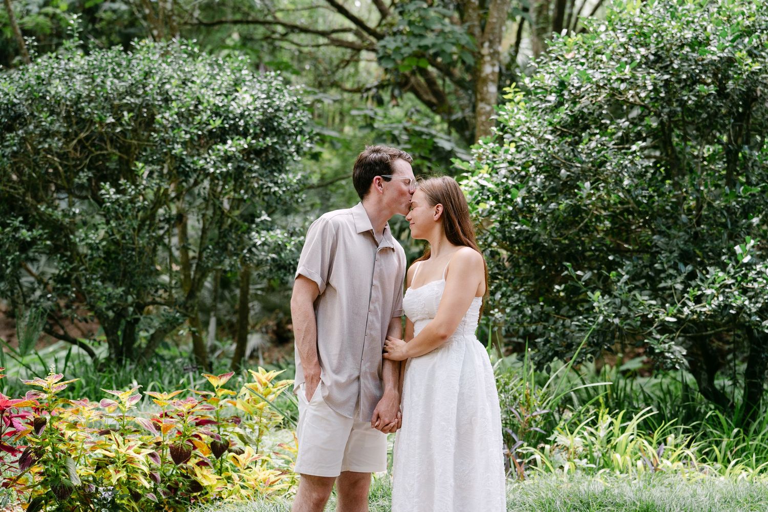 Couple holding hands and sharing a romantic moment in a lush tropical garden with vibrant greenery.