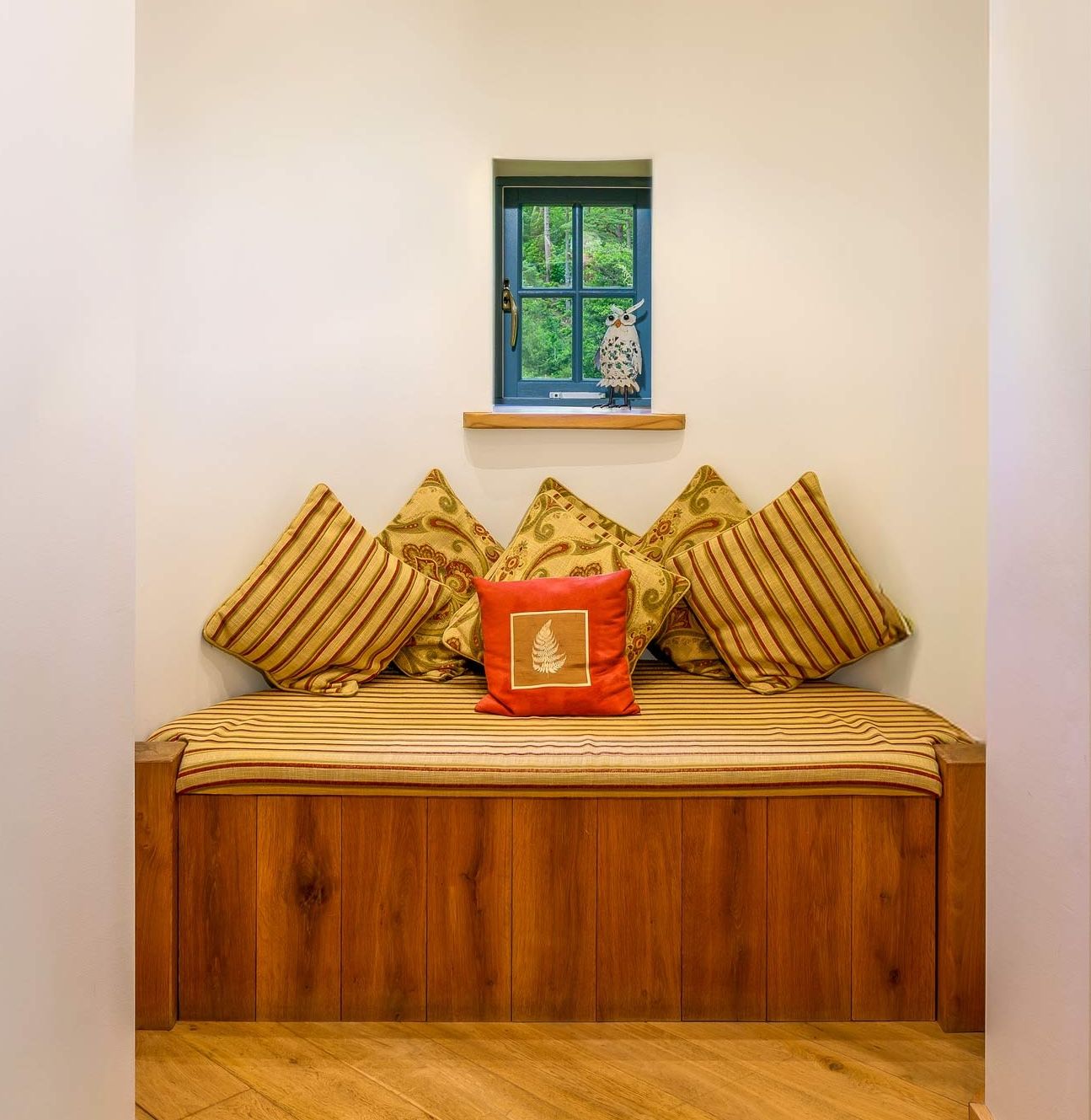 Cosy wooden daybed nook with striped throw pillows and a small square window above.