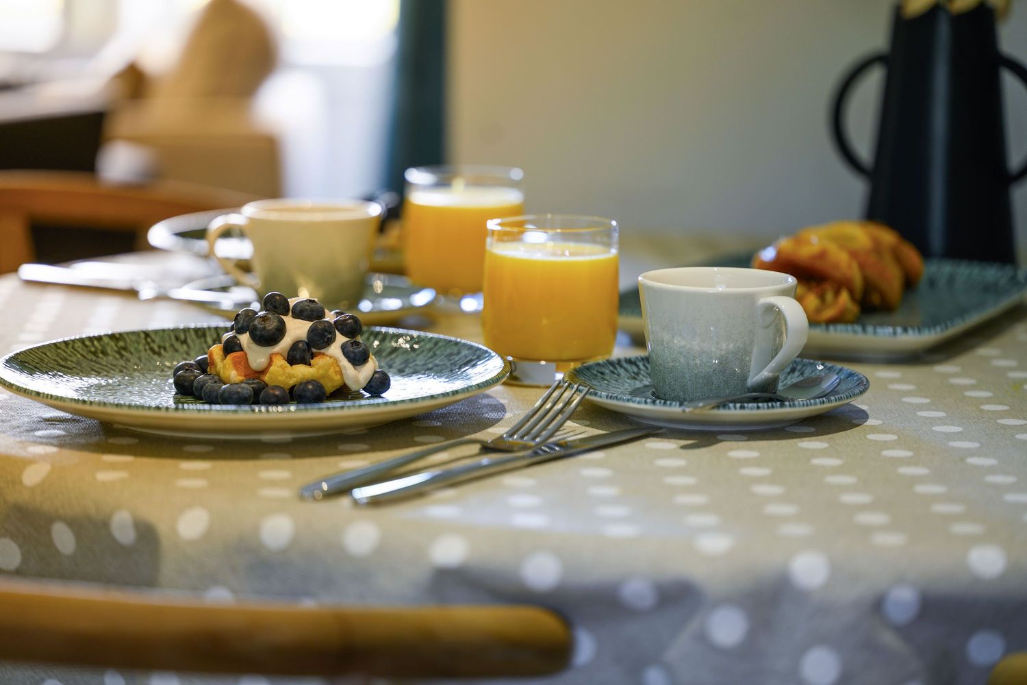 Breakfast image showing orange juice, pancakes, blueberries, coffee cups in a cosy Airbnb.