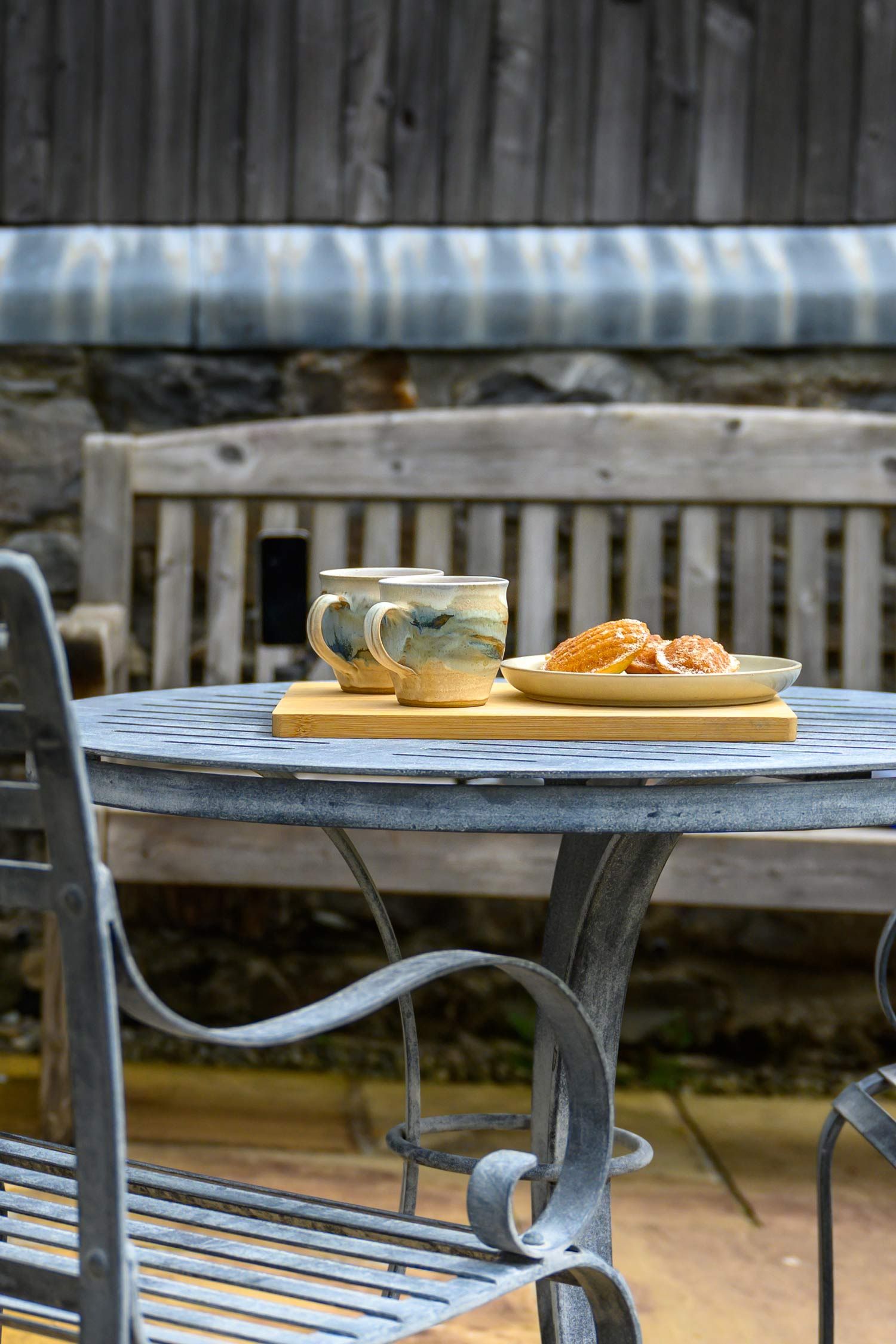 Outdoor patio table set with two mugs and snacks on a wooden tray.