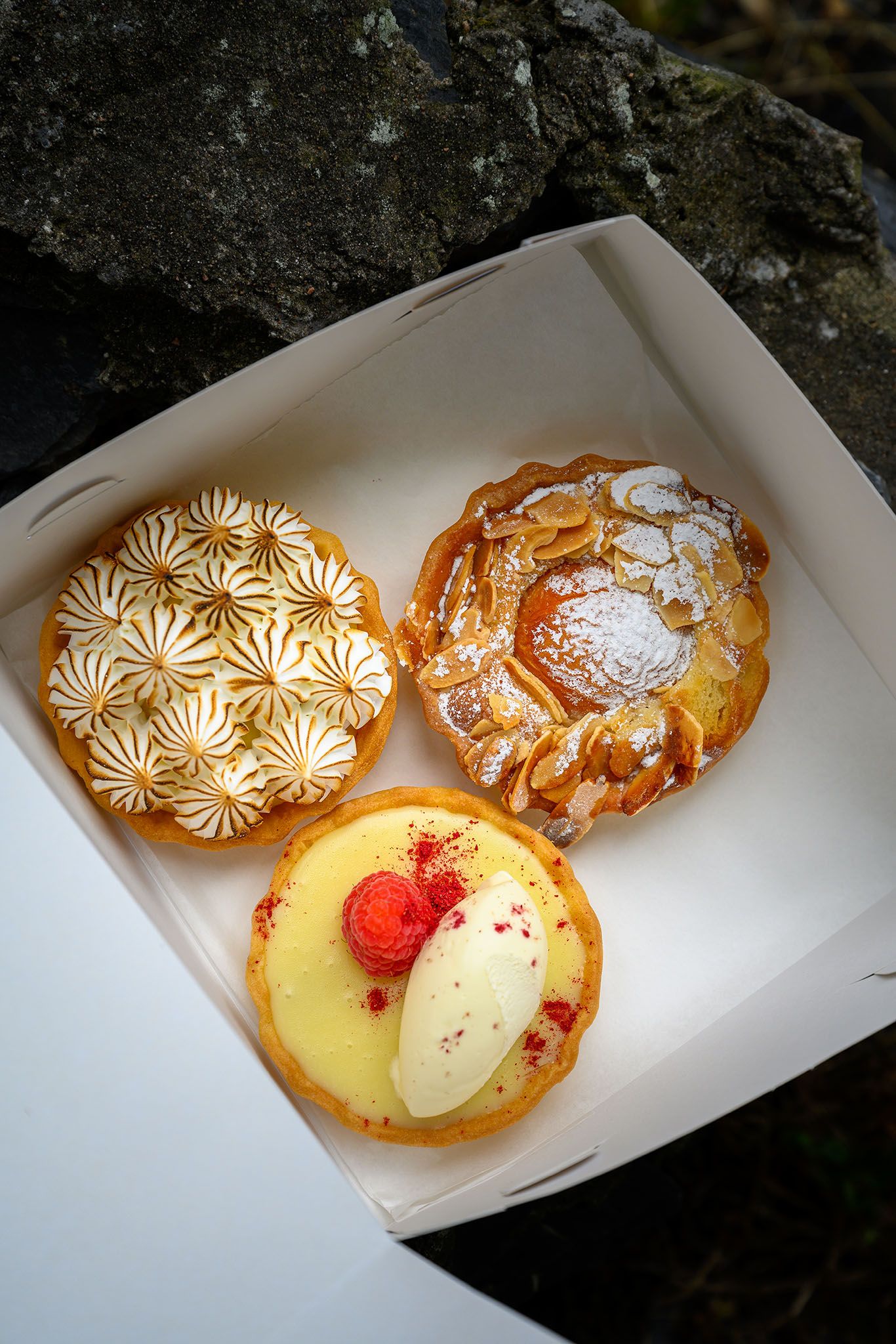 Box of freshly made pastries including meringue tarts and glazed pastries at a café pâtisserie in Glencoe, Scotland.