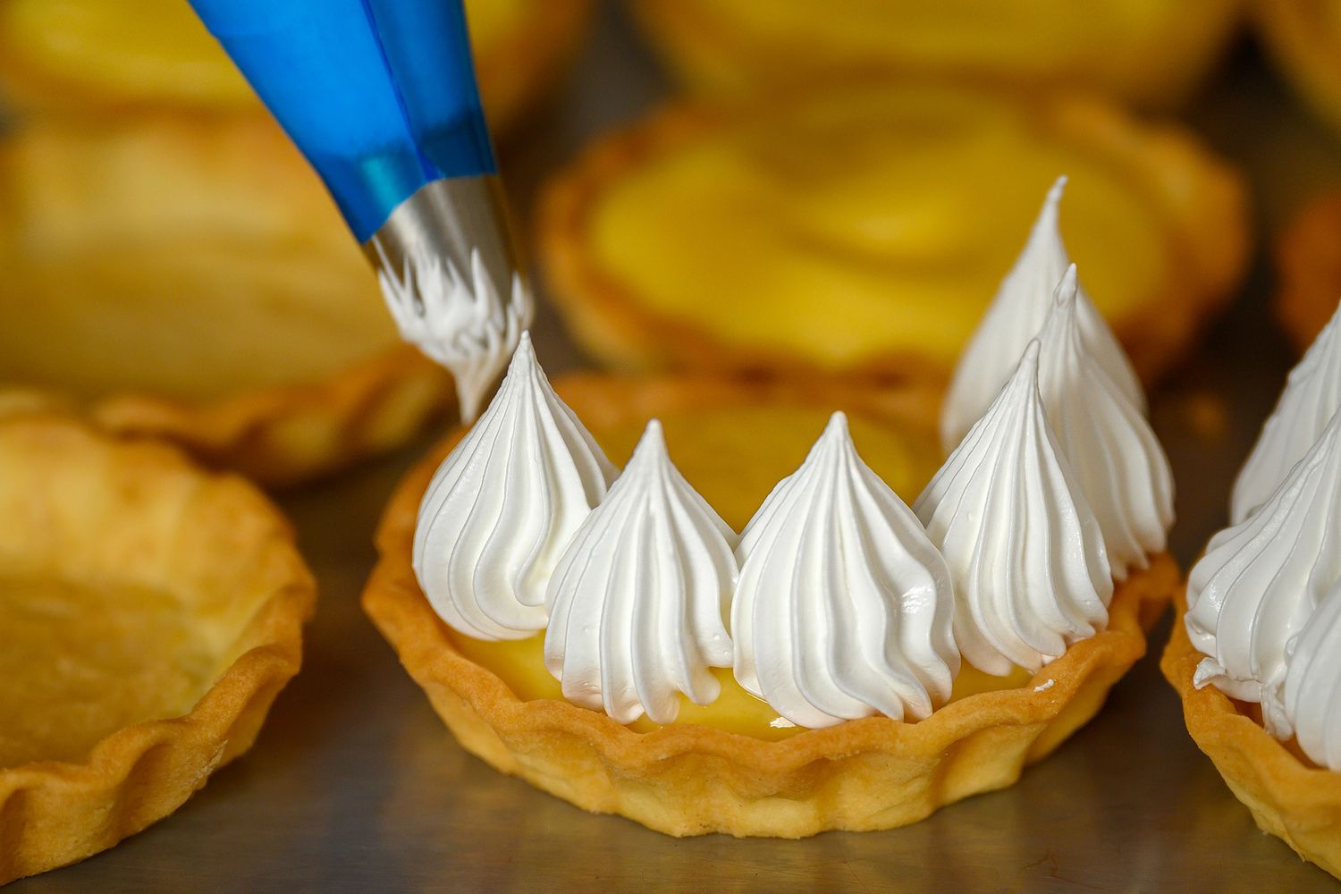 Pastry chef piping meringue onto a freshly baked tart at a café pâtisserie in Glencoe, Scotland.