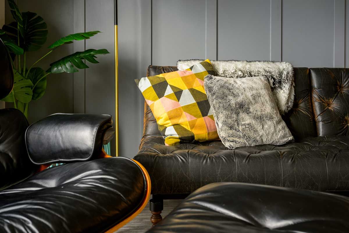 Close-up of a black leather sofa and armchair with a geometric yellow cushion and textured grey throw pillow.