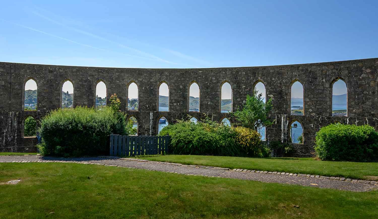 McCaig's Tower, a prominent stone arch landmark overlooking grassy lawns in Oban, Scotland.